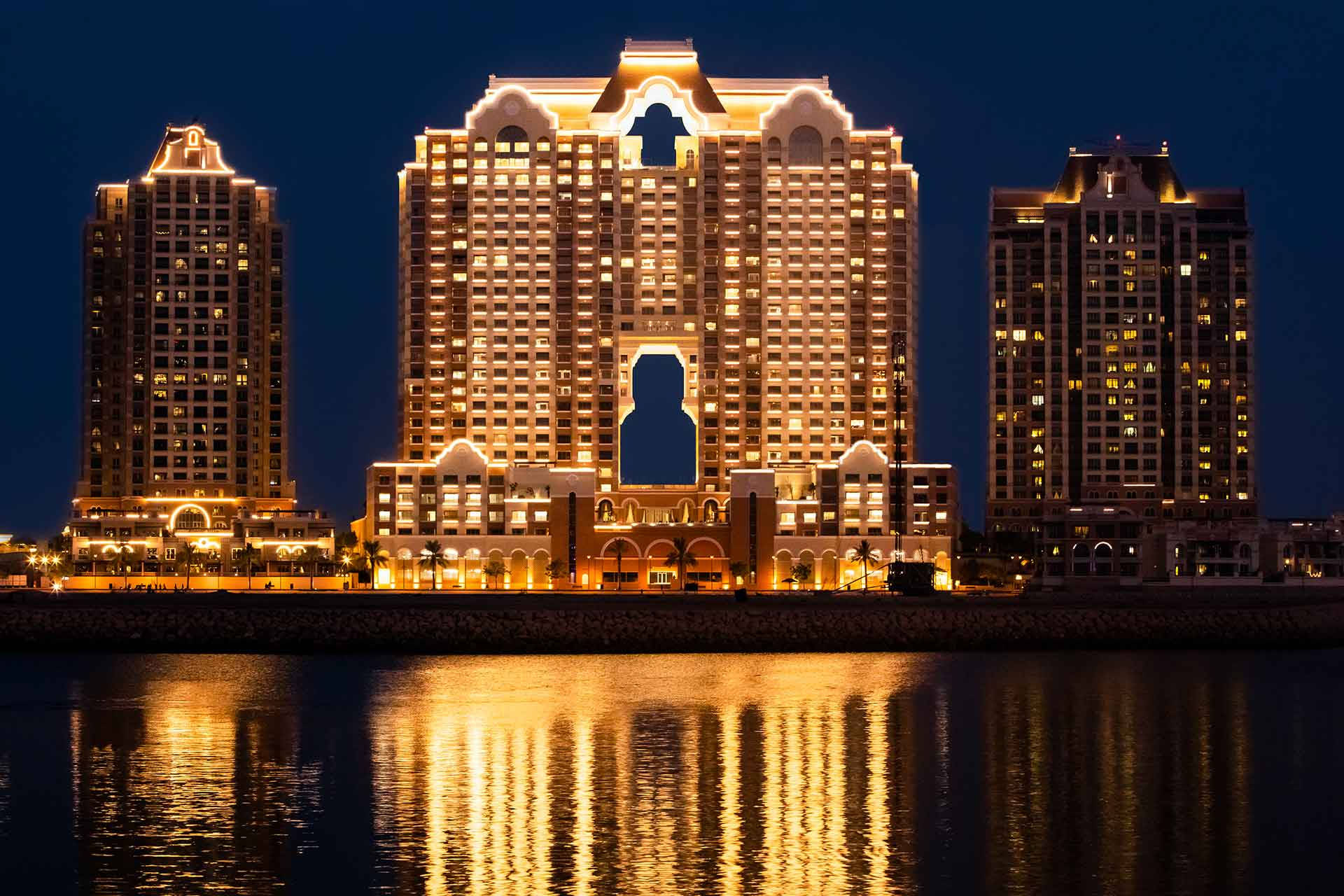 Qatar 桌布 壁紙 — 在深邃的夜空下，宏偉的燈光酒店塔樓溫暖地倒映在平靜的水面上。
