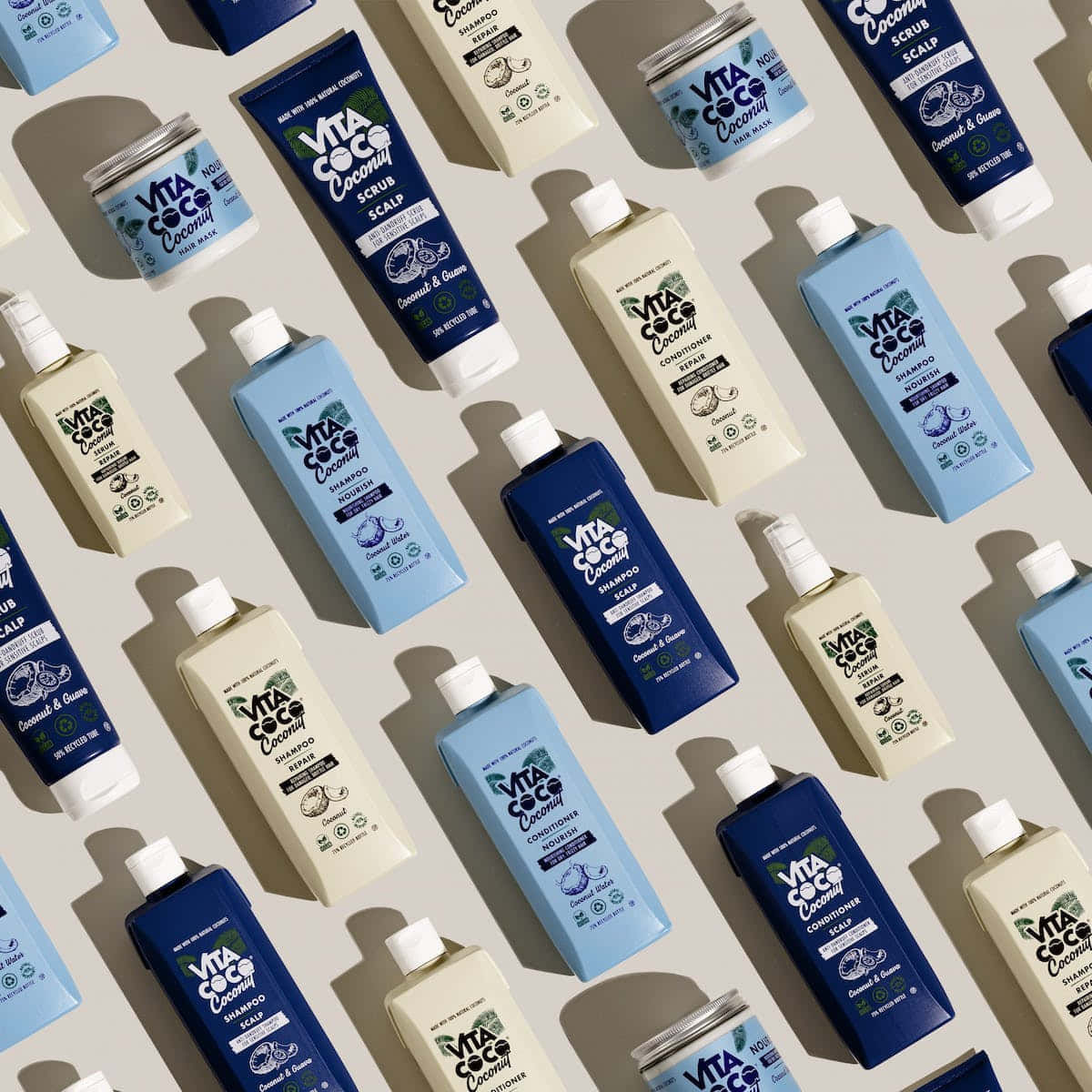 Haircare 桌布 壁紙 — 在淺米色表面上對角排列的藍色和奶油色瓶裝Vita Coco椰子護髮產品的平鋪佈局。