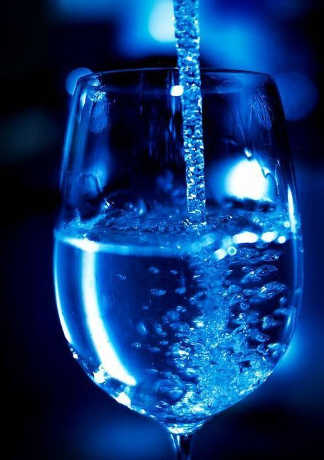 dark blue aesthetic tumblr 桌布 壁紙 — 在清涼藍光下，氣泡水倒入玻璃杯的特寫，帶有鮮明的氣泡和反射。