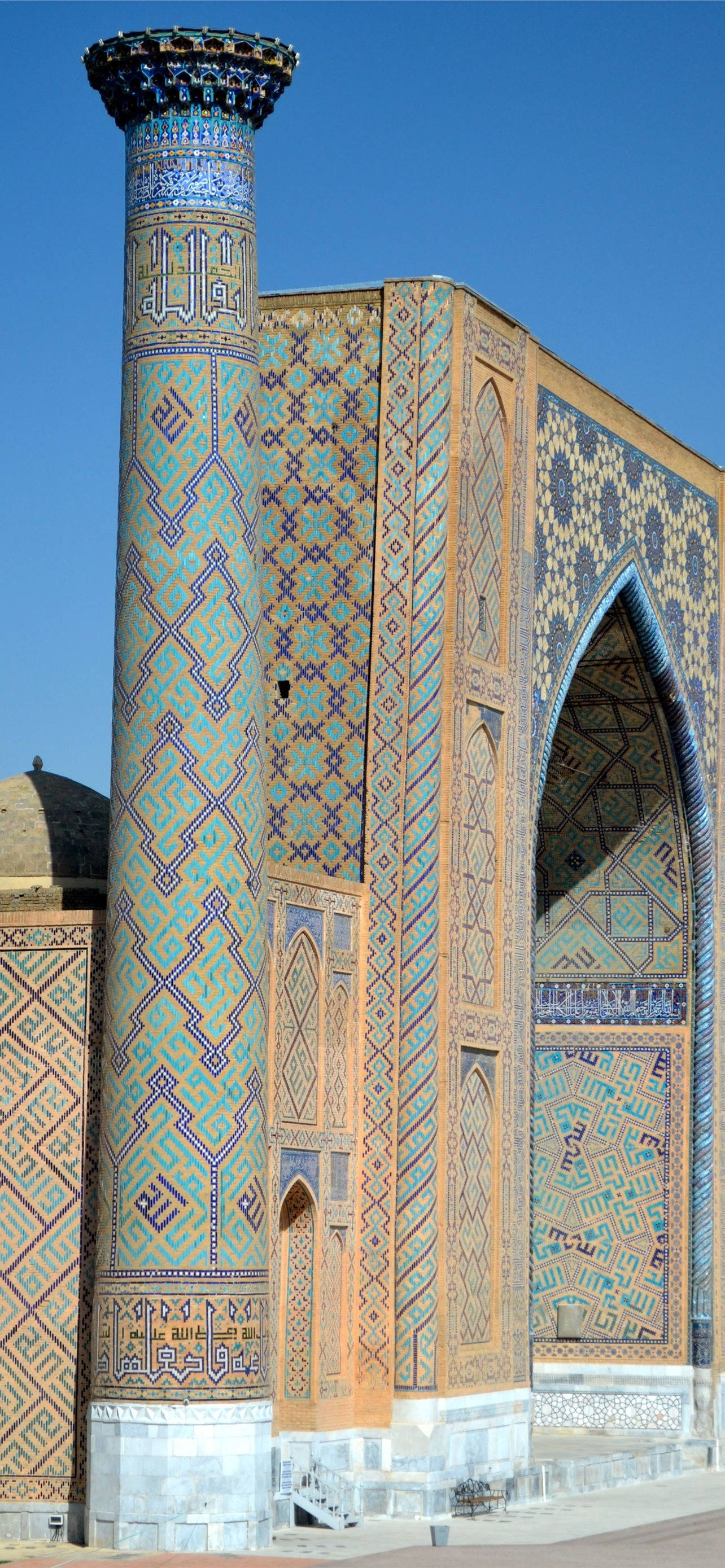 Uzbekistan 桌布 壁紙 — 在清澈的藍天下，一座高聳的宣禮塔和華麗的清真寺外牆覆蓋著複雜的藍綠色和金色幾何瓷磚。