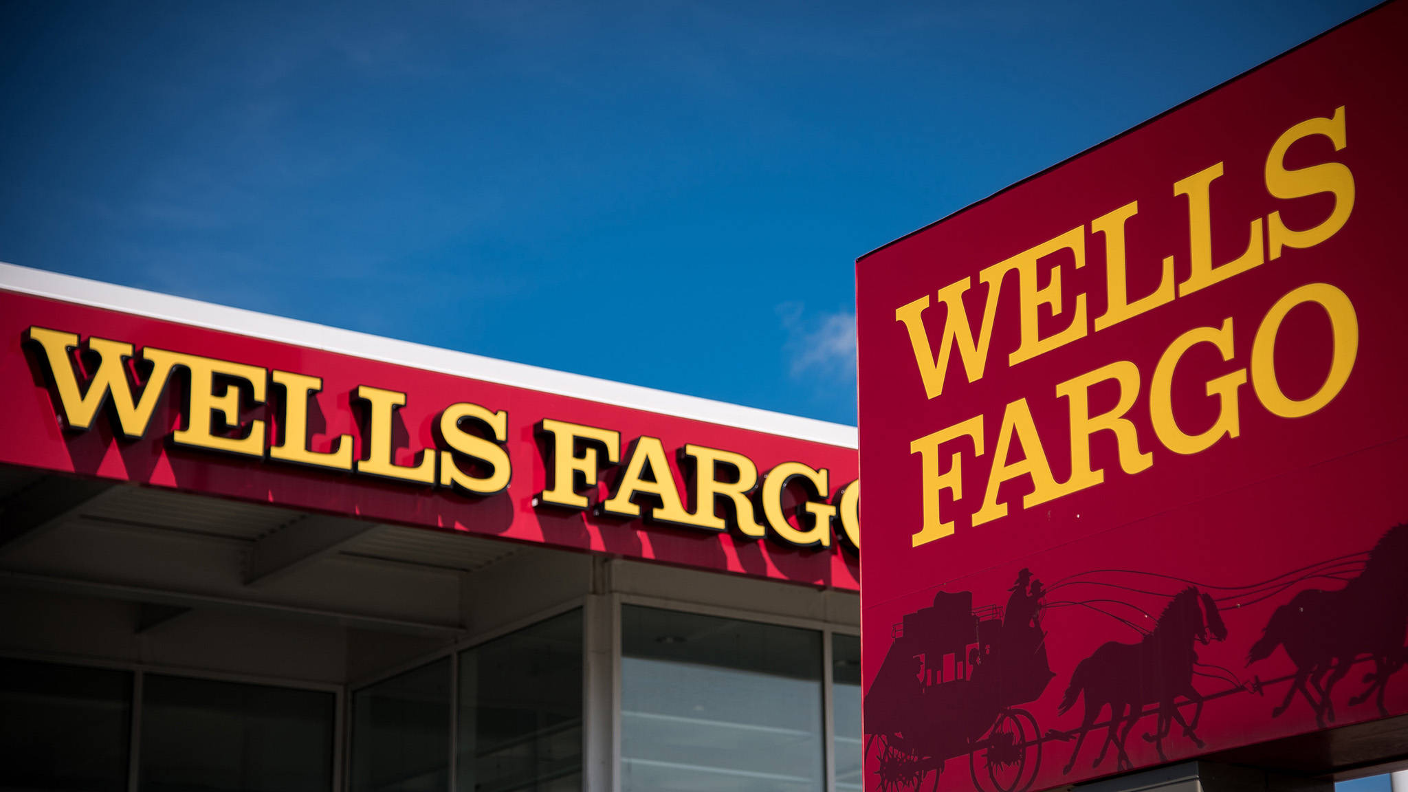 sign 桌布 壁紙 — 在清澈的藍天下，大膽的紅色 Wells Fargo 標誌配上黃色字體和馬車剪影。