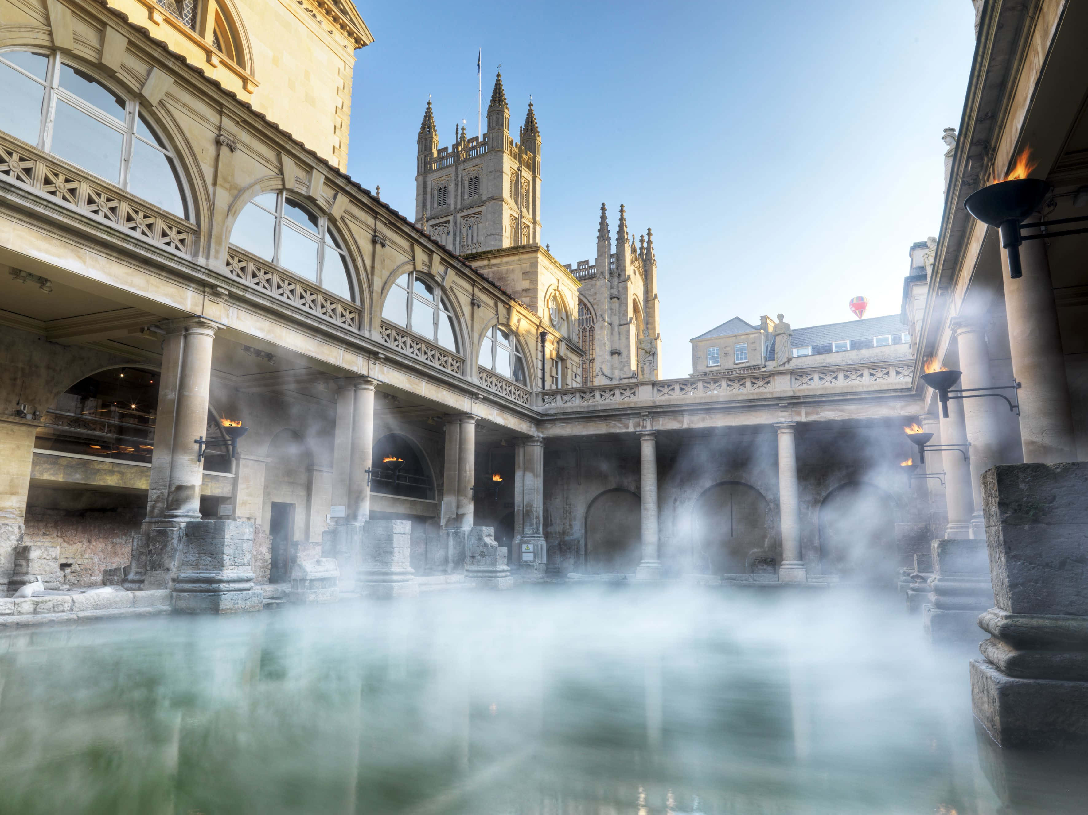 England 桌布 壁紙 — 在清澈的藍天下，蒸氣從被石柱和拱門環繞的歷史羅馬浴場升起。
