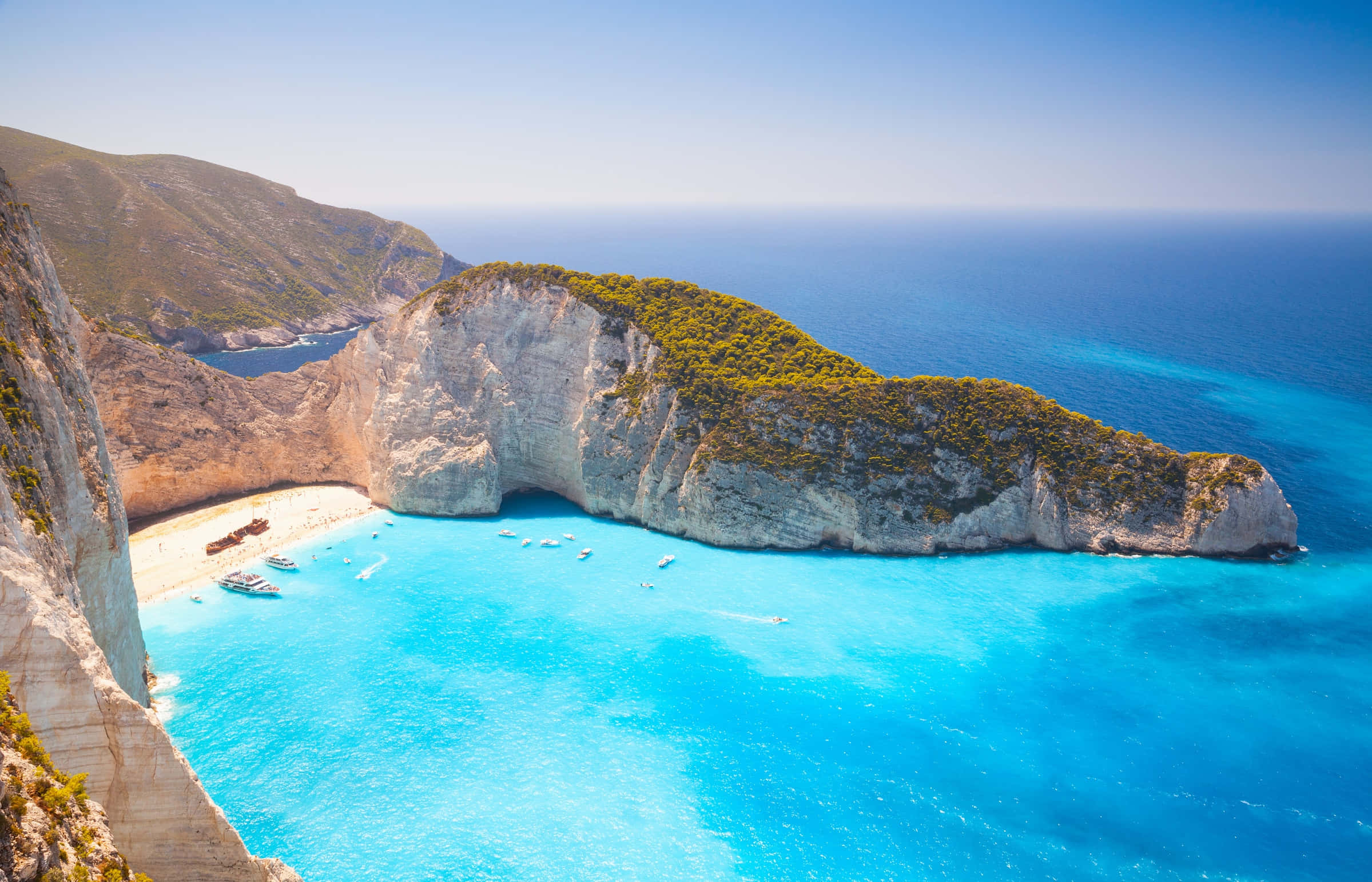 Greek Beach 桌布 壁紙 — 在清澈藍天下，納瓦吉奧海灘的鳥瞰圖，呈現碧綠海水、船隻和白色懸崖。