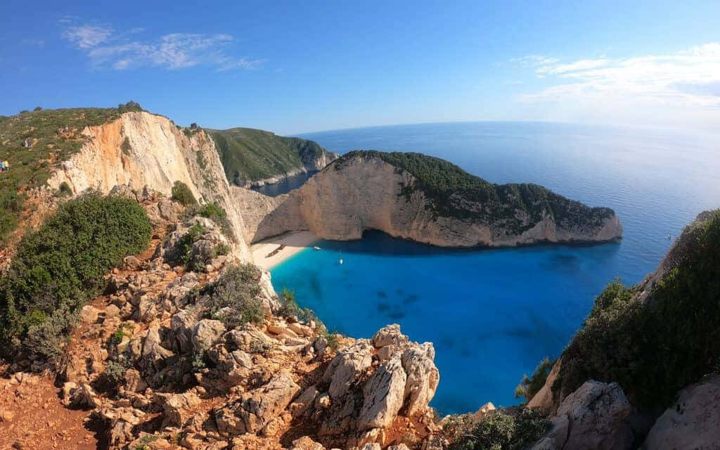 Greek Island 桌布 壁紙 — 在清澈藍天下，高聳懸崖之間環抱著碧綠海水的納瓦吉奧海灘，景色令人嘆為觀止。