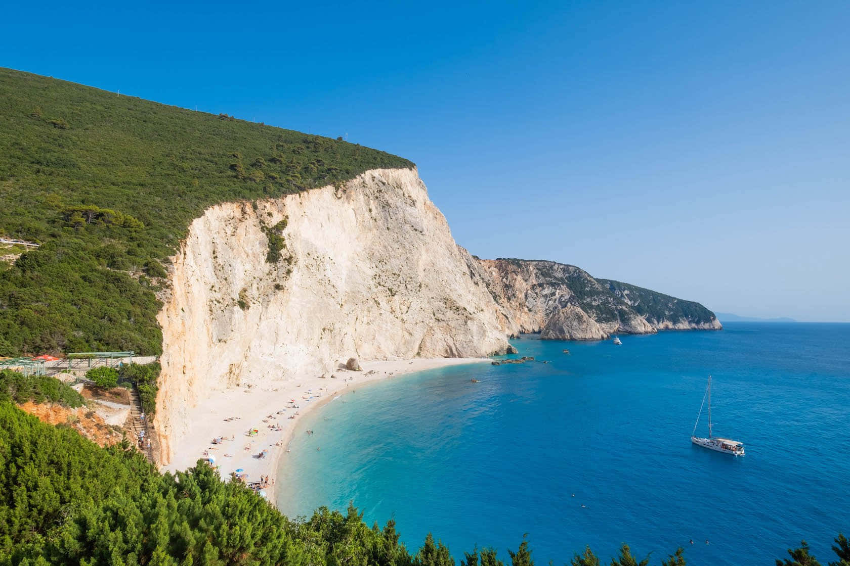 Greek Beach 桌布 壁紙 — 在清澈藍天下，高聳白色懸崖之間環抱著一個迷人的海岸小海灣，海水呈藍綠色。