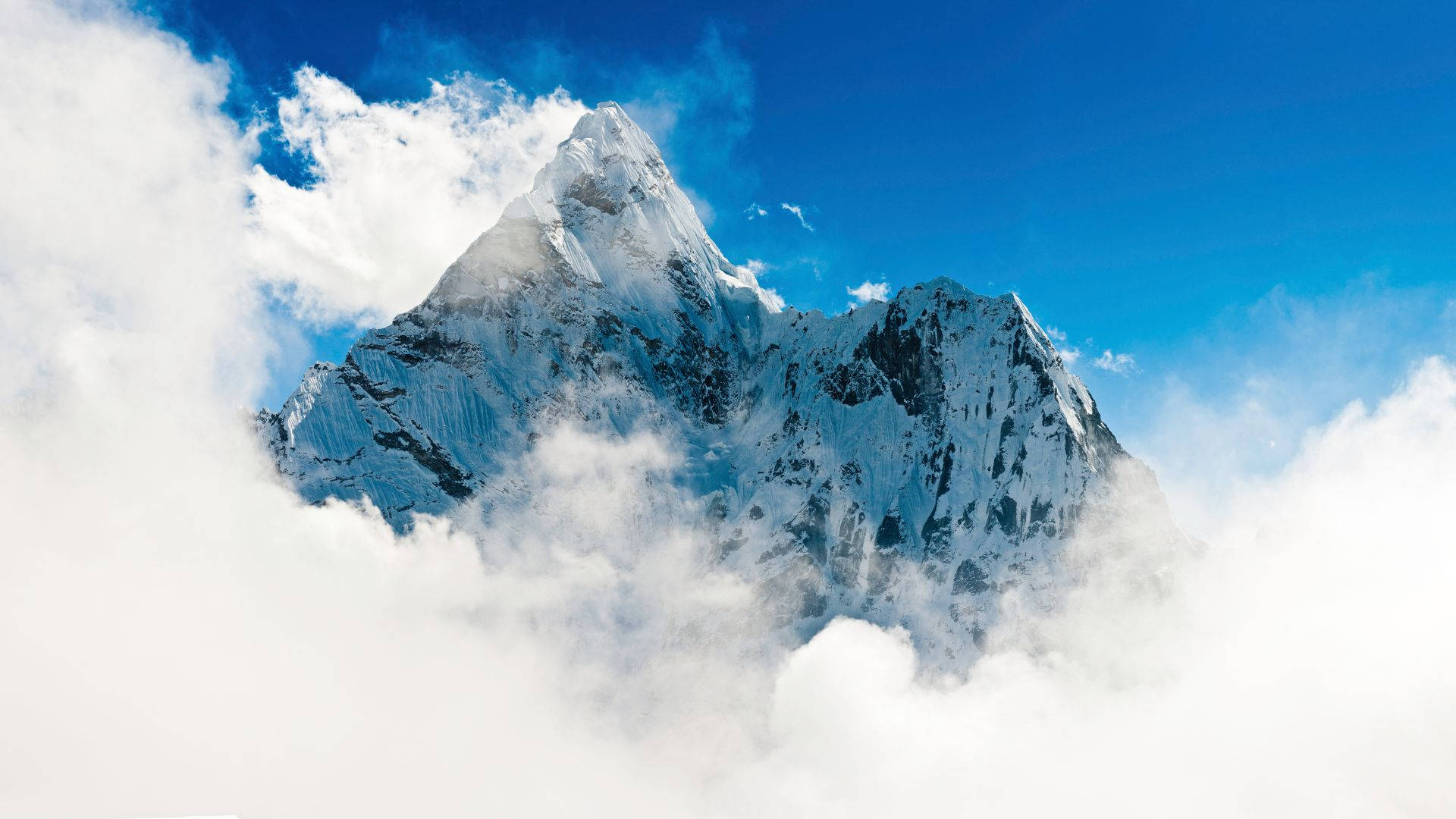 高清 桌布 壁紙 — 在湛藍的天空下，雄偉的雪山峰頂穿過蓬鬆的白雲。