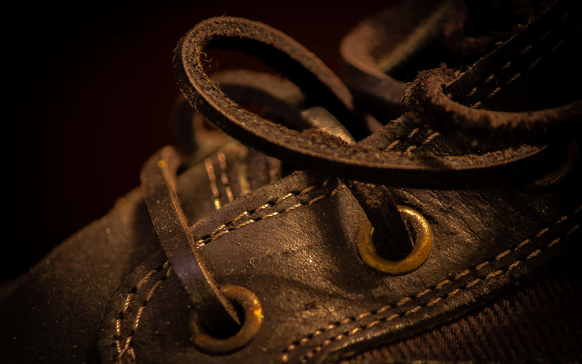 Footwear Design 桌布 壁紙 — 在溫暖戲劇性燈光下，一雙磨損的皮鞋特寫，帶有磨損的鞋帶和金色鞋眼。
