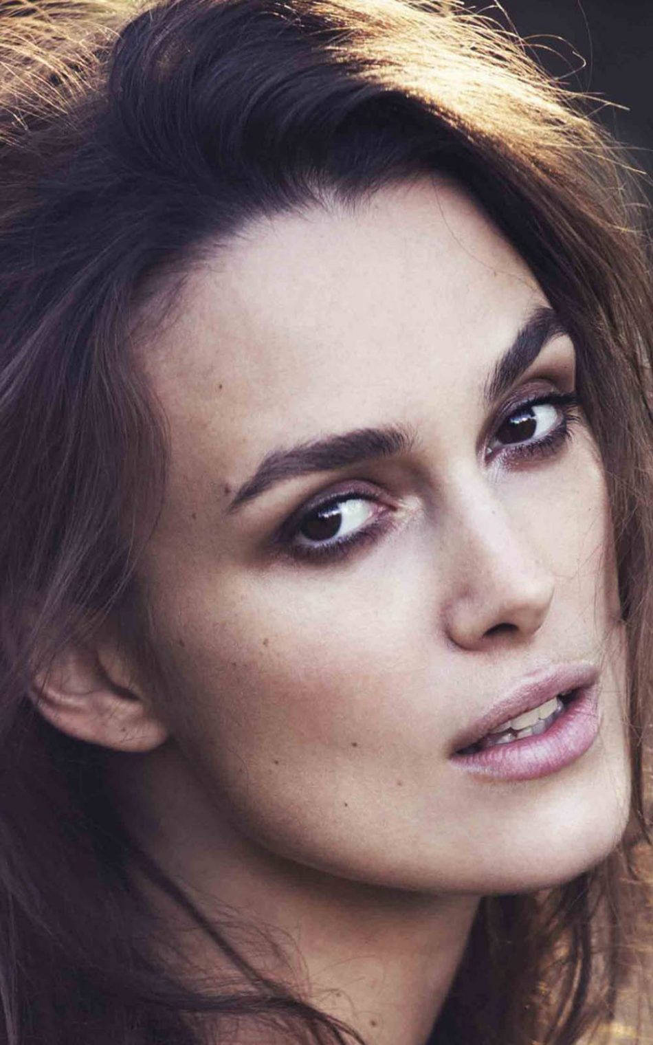 Keira Knightley 桌布 壁紙 — 在溫暖燈光下，一位深色頭髮、眼神強烈的女性的特寫肖像。