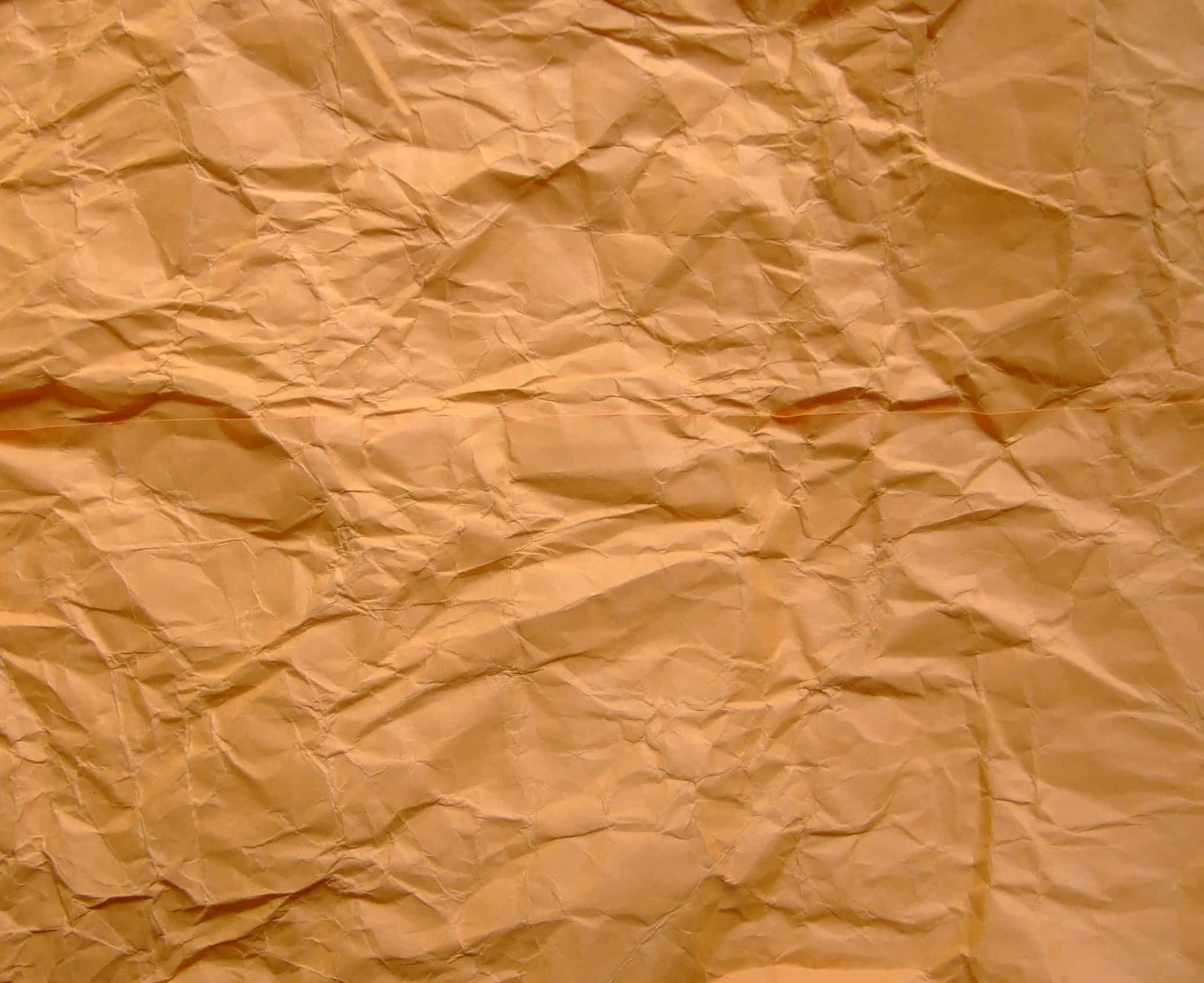 Old Paper 桌布 壁紙 — 在溫暖燈光下，帶有深摺痕和柔和陰影的皺褶金棕色紙張特寫。