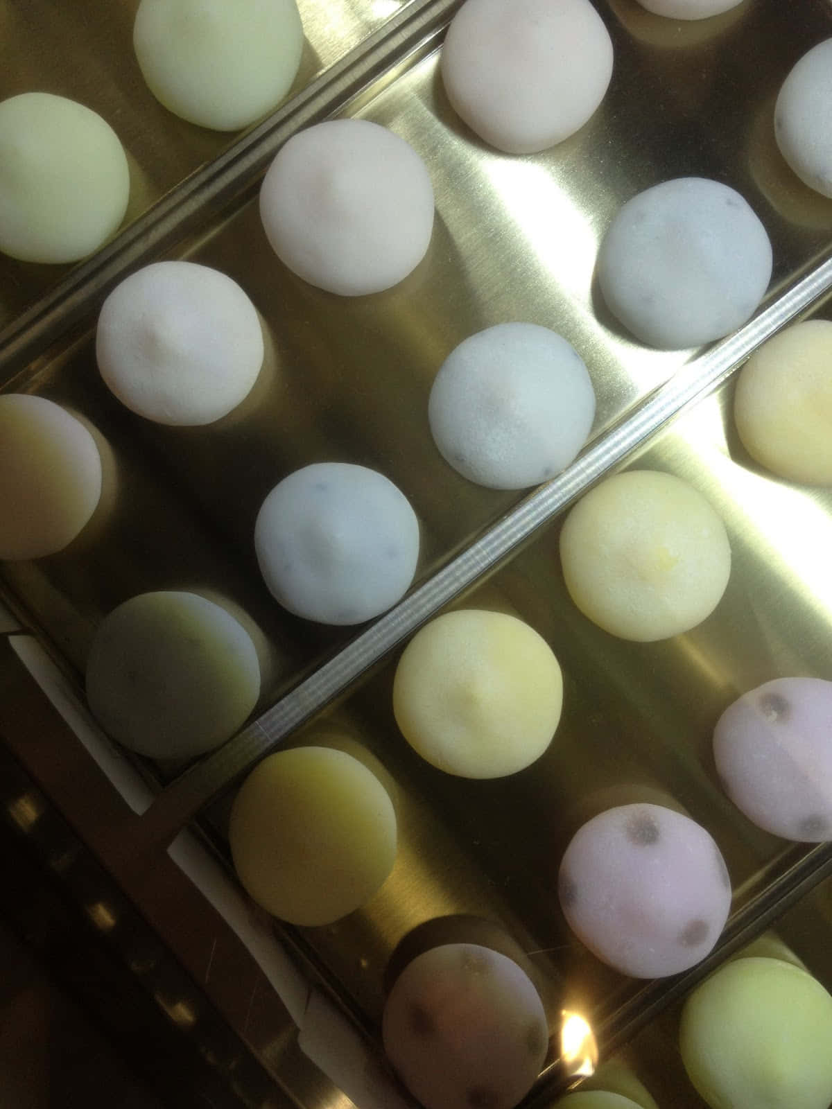 Japanese Sweets 桌布 壁紙 — 在溫暖燈光下，閃閃發光的金色托盤上排列著一排排粉彩色的麻糬球。