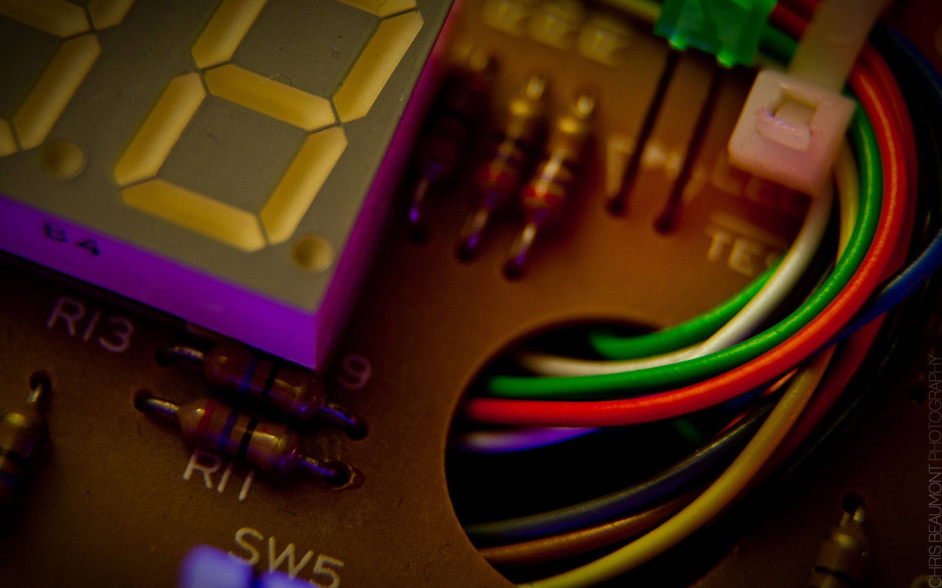 Electronics 桌布 壁紙 — 在溫暖燈光下，電路板上發光的黃色數位顯示器特寫，帶有彩色電線和標籤電阻。