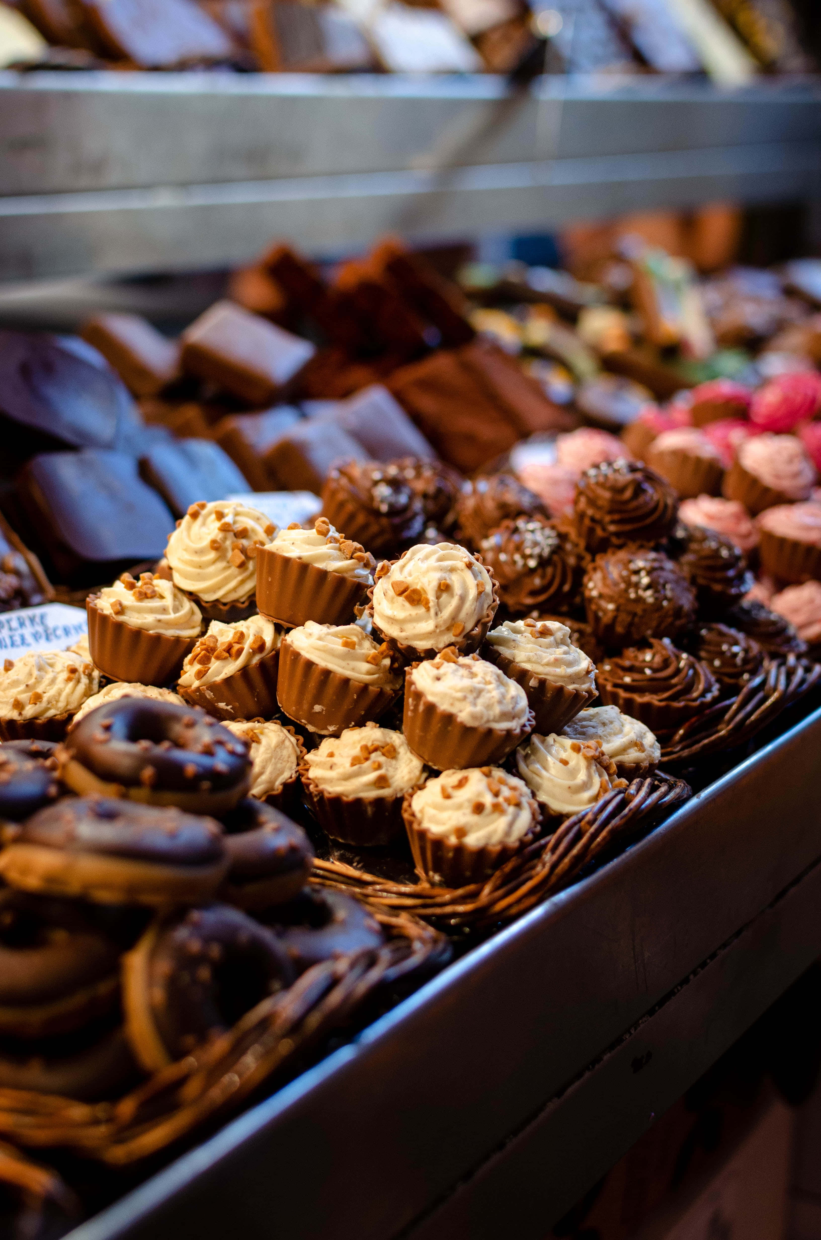 Bakery 桌布 壁紙 — 在溫暖燈光下，麵包店陳列櫃中籃子裡擺放著誘人的各式巧克力和糕點。