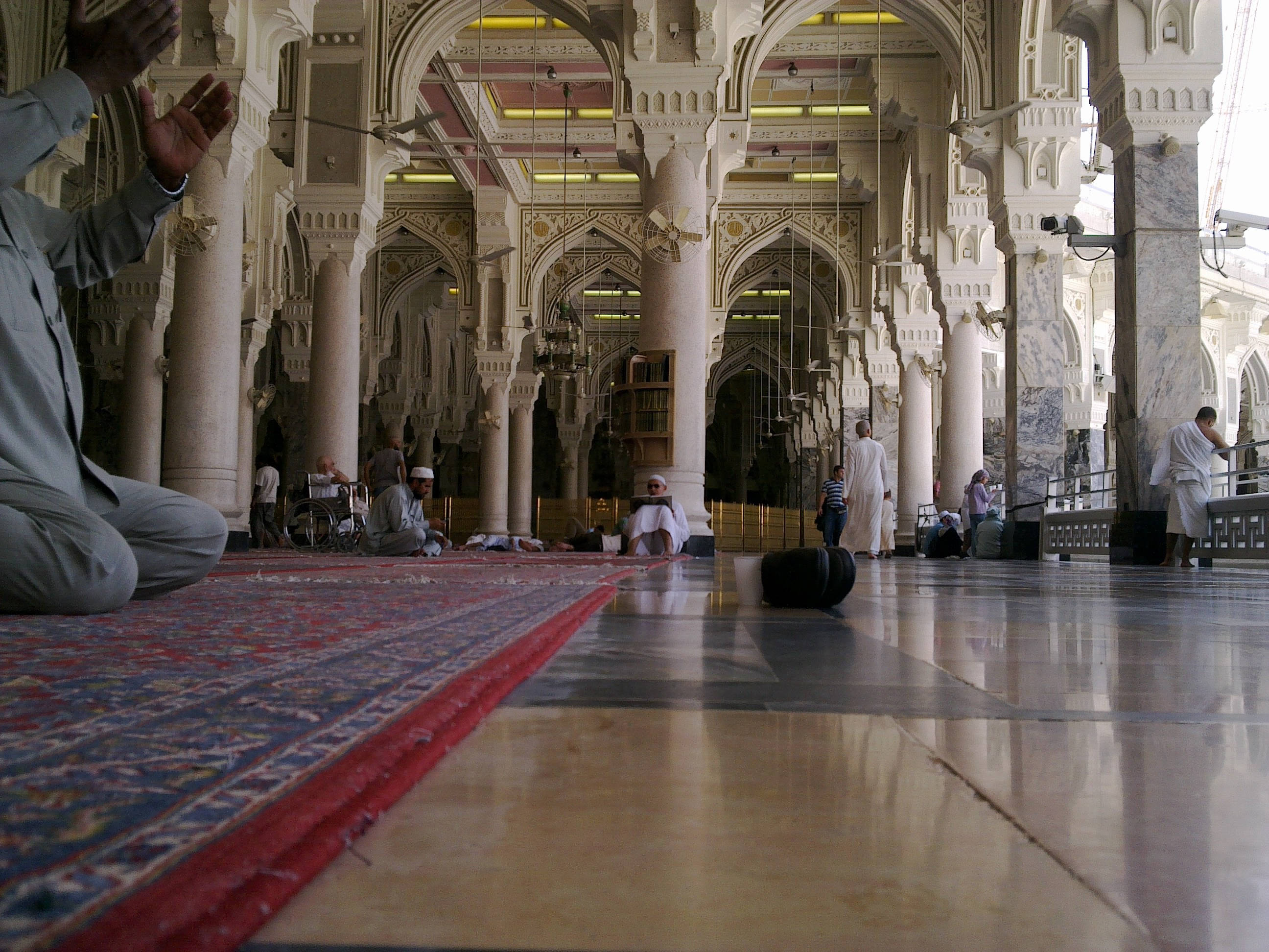 Makkah 桌布 壁紙 — 在溫暖的人造燈光下，祈禱在一座擁有大理石柱和複雜拱門的大清真寺中展開。