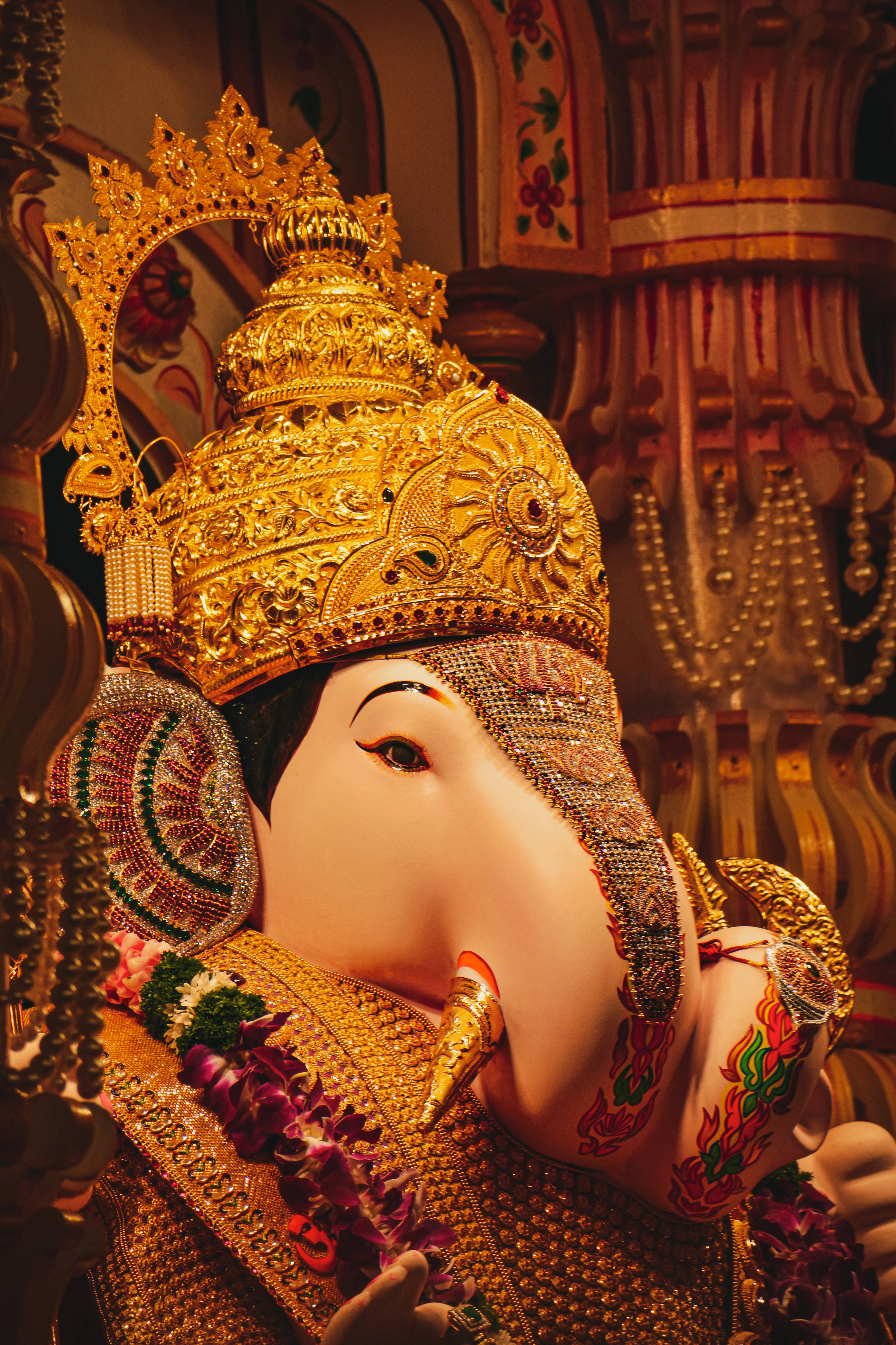 ganesh 4K 桌布 壁紙 — 在溫暖的寺廟燈光下，一尊裝飾華麗的金色象神雕像，帶有精緻的珠寶和花環的特寫。