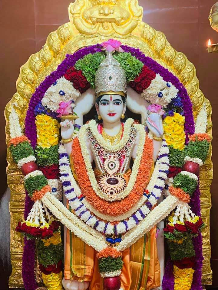 Satyanarayana Swamy 桌布 壁紙 — 在溫暖的寺廟燈光下，一尊閃耀的印度教神像裝飾著鮮豔的花環和金飾。