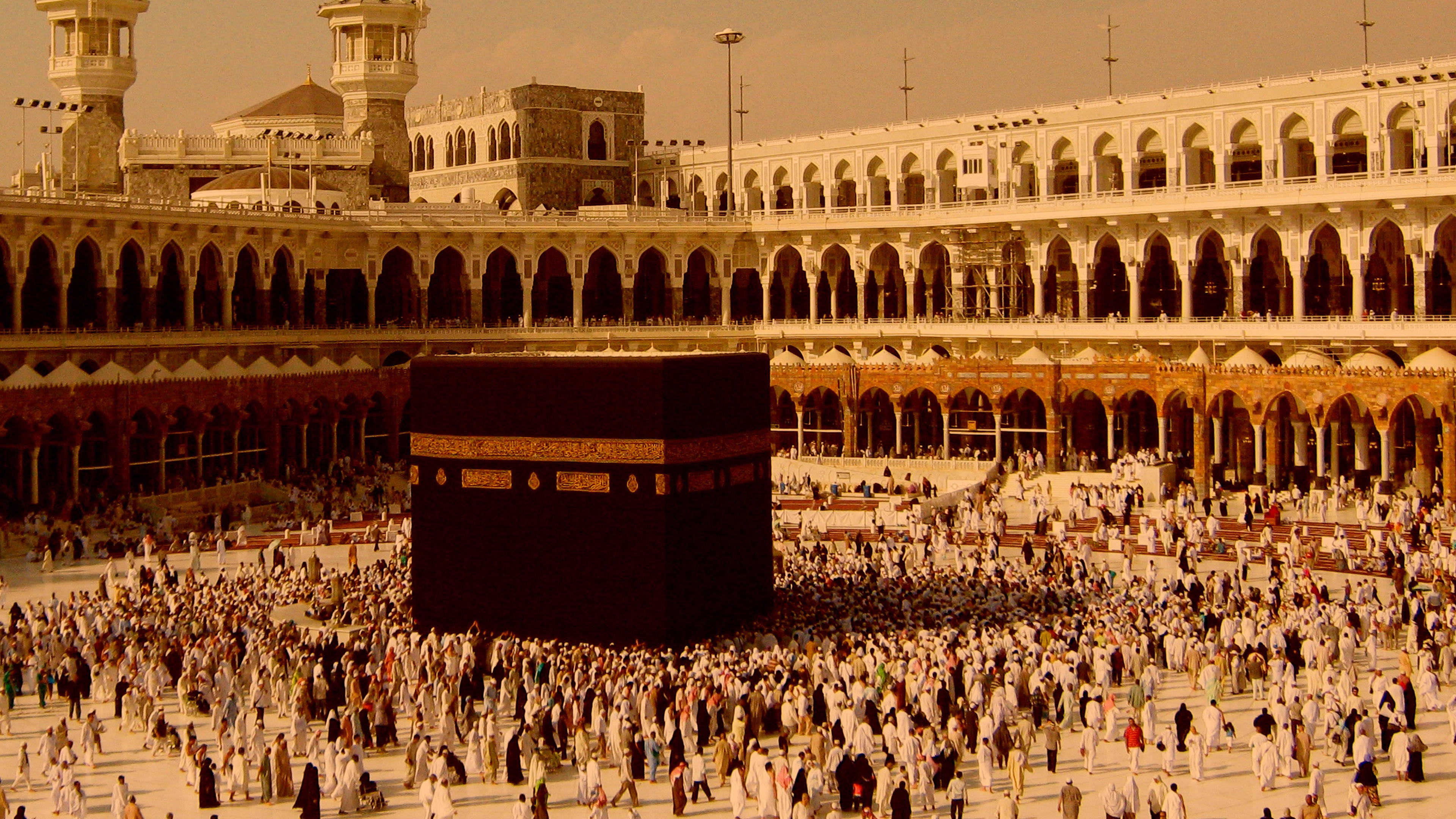 muslim 桌布 壁紙 — 在溫暖的金色天空下，大批朝聖者在麥加大清真寺的廣闊庭院中繞行黑色天房。