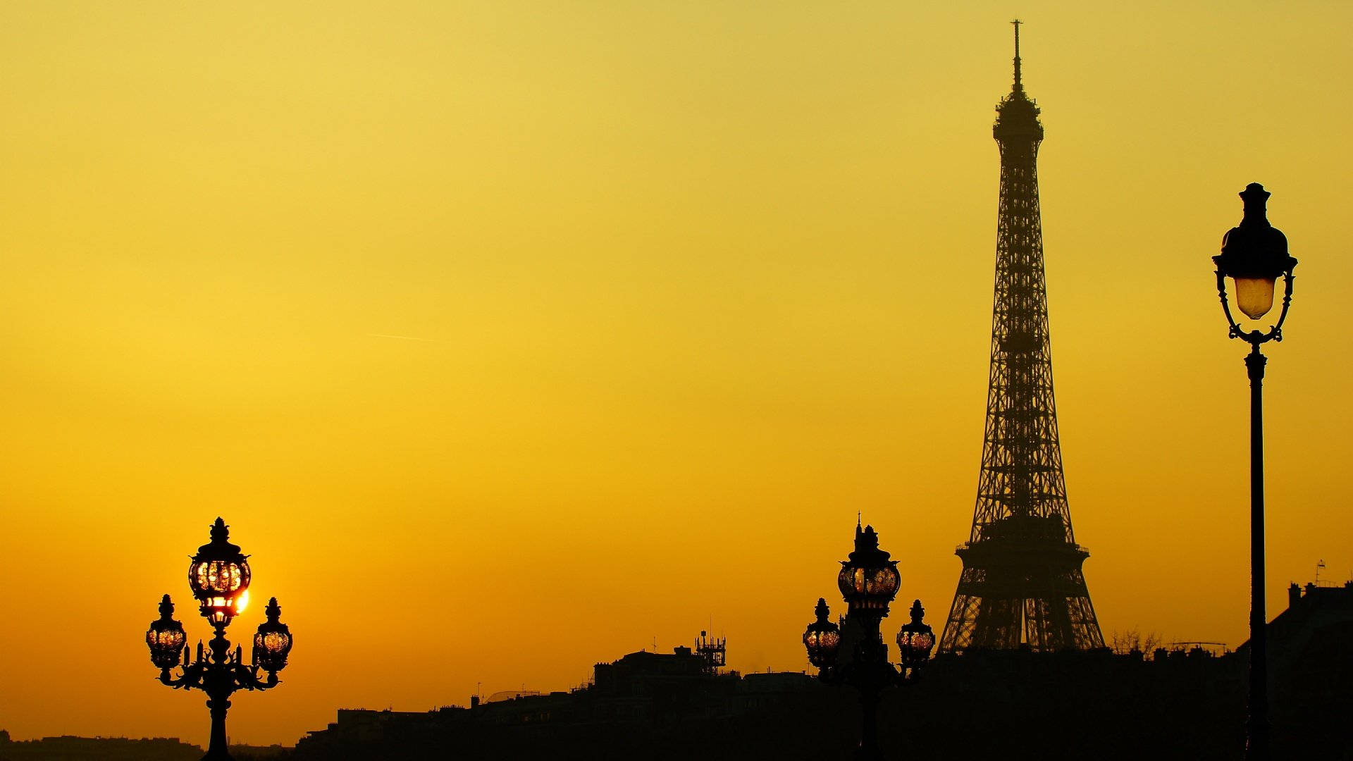 Eiffel Tower 桌布 壁紙 — 在溫暖的金色日落天空襯托下，艾菲爾鐵塔和華麗路燈的剪影。