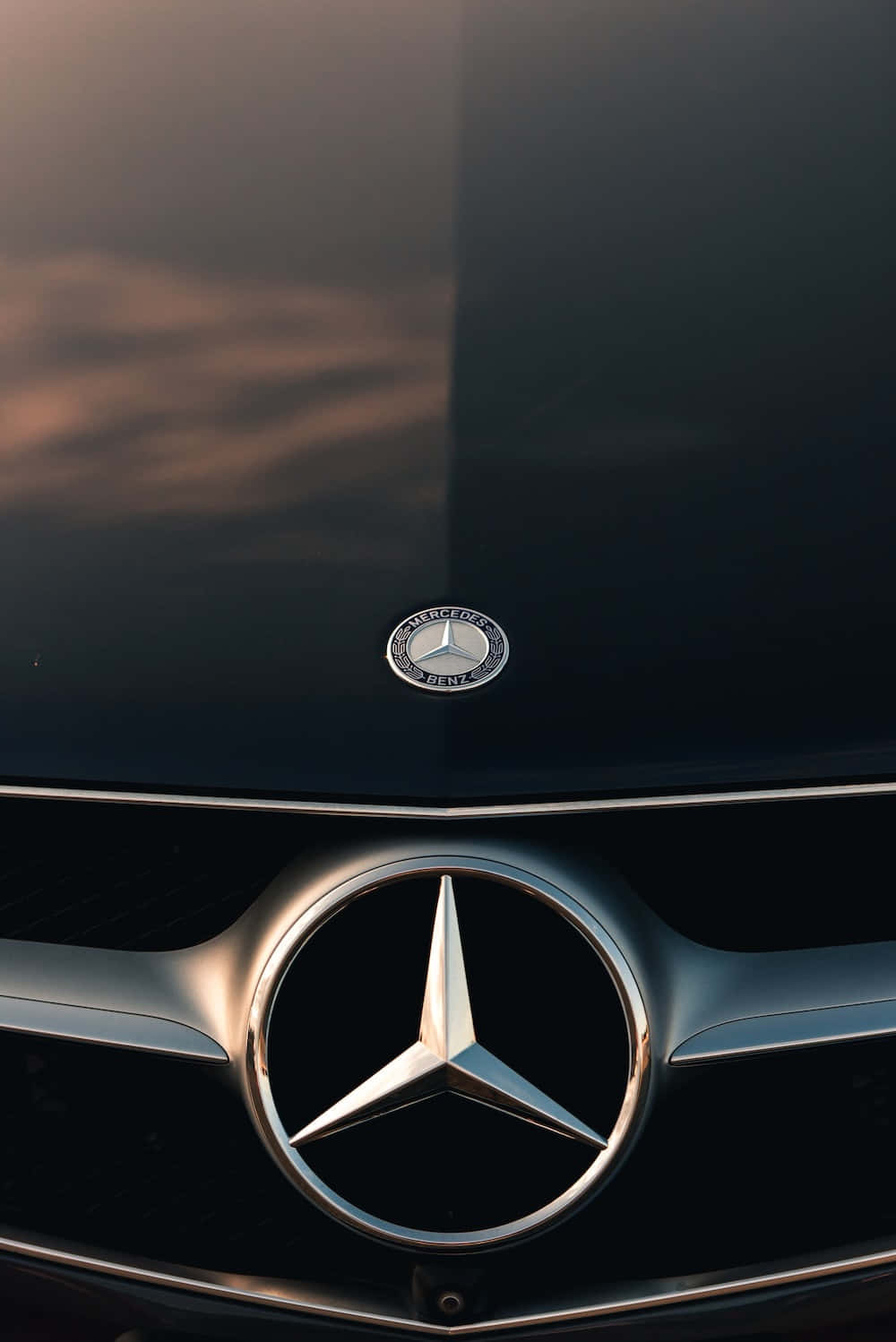 Mercedes 桌布 壁紙 — 在溫暖的金色時刻光線下，時尚黑色賓士水箱護罩和引擎蓋標誌的特寫。