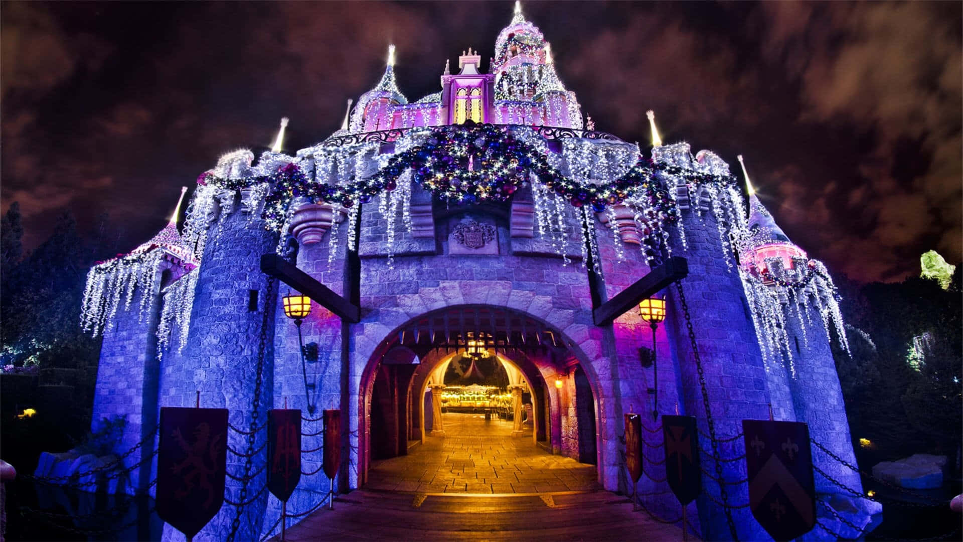 Disney Castle 桌布 壁紙 — 在漆黑的夜空下，宏偉的城堡拱門裝飾著發光的紫色和白色燈光以及冰柱裝飾。