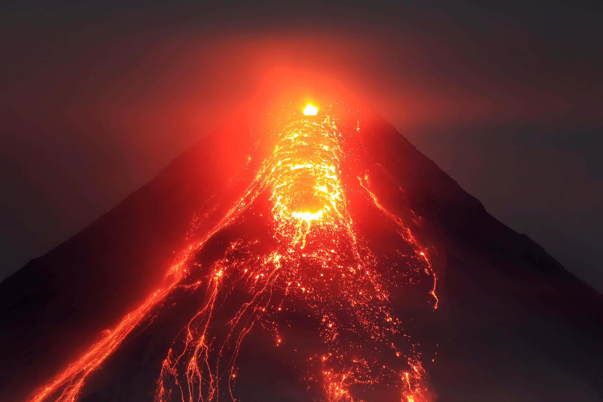 Volcano 桌布 壁紙 — 在漆黑的夜空下，火山在夜間爆發，熾熱的熔岩沿著山坡流下。