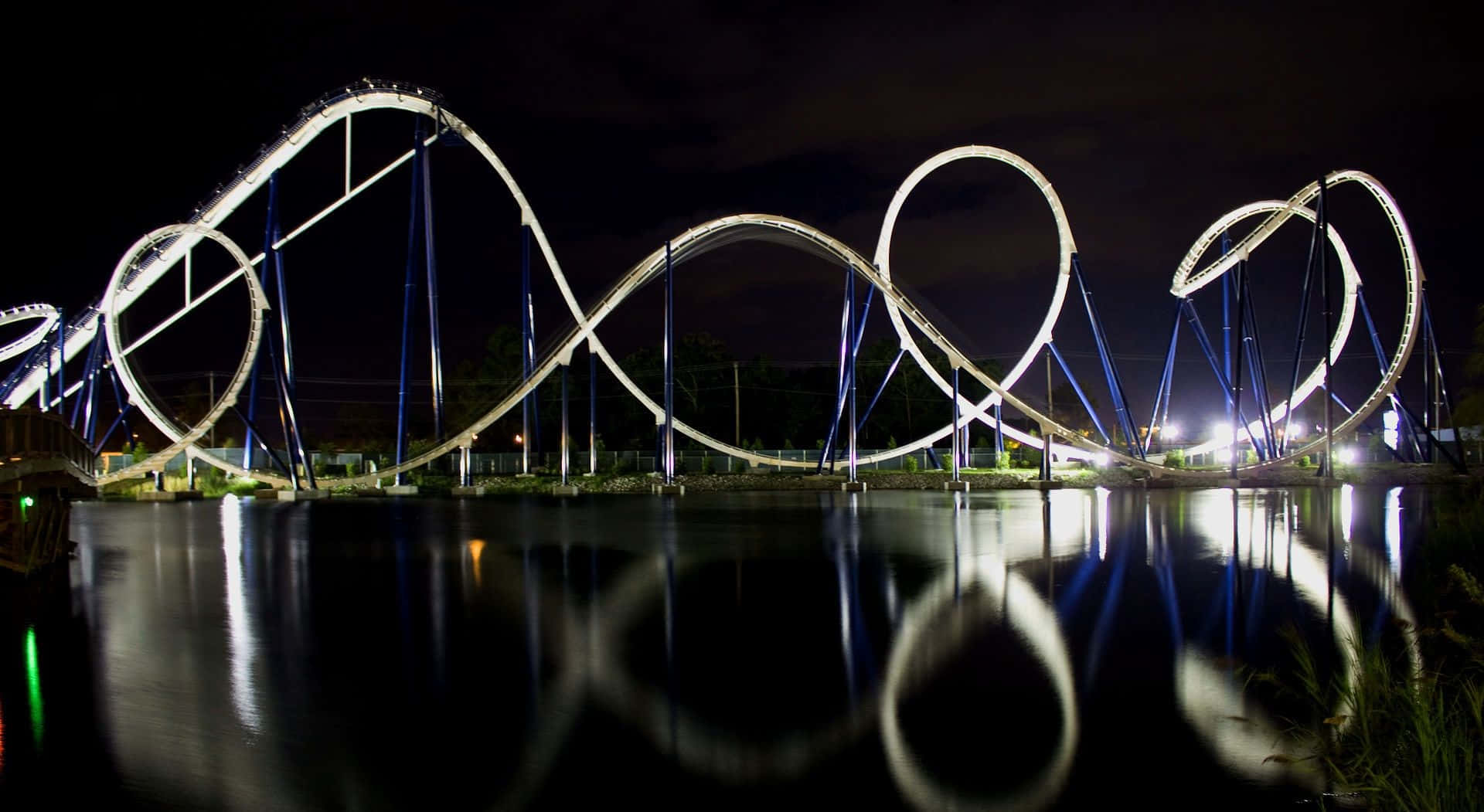 Roller Coaster 桌布 壁紙 — 在漆黑的夜空下，閃閃發光的雲霄飛車完美地倒映在平靜的水面上。