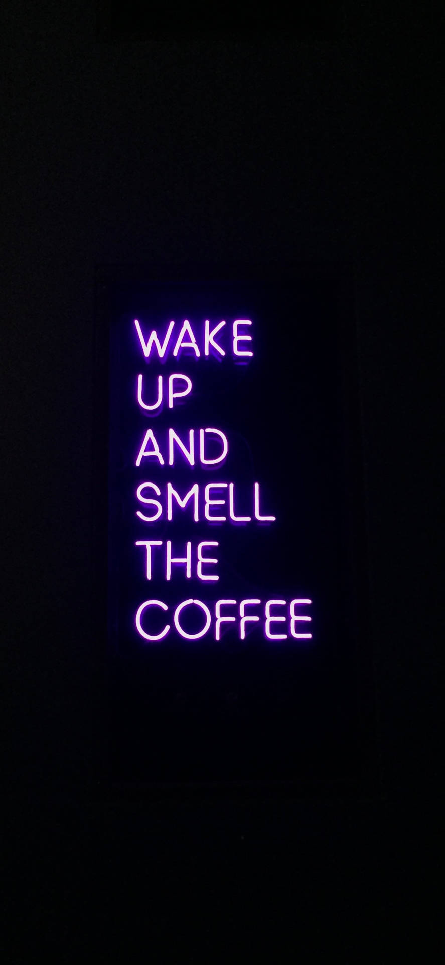 在黑暗房間中，一個寫著 wake up and smell the coffee 的紫色霓虹燈牌。