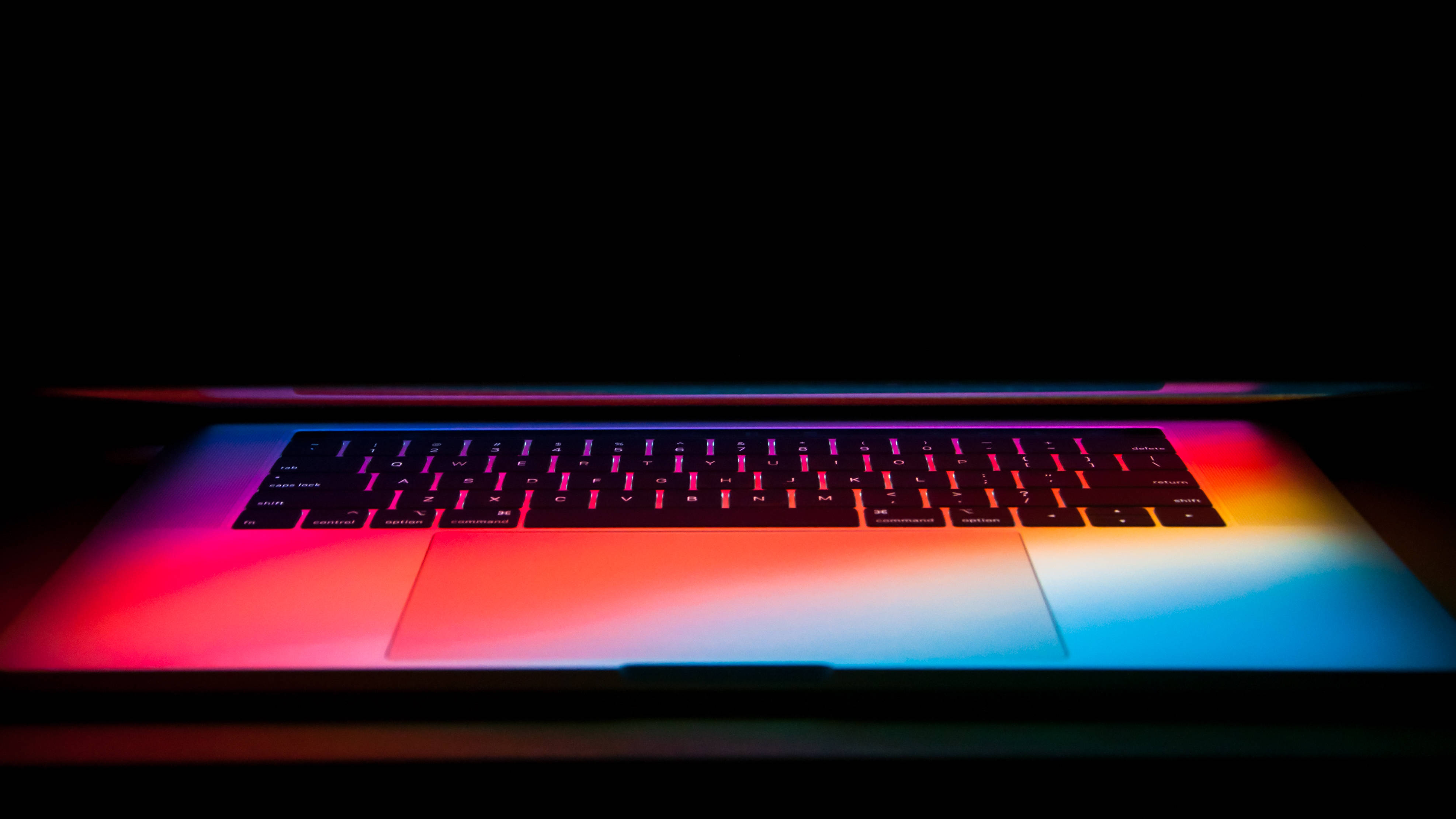 Mac Os 桌布 壁紙 — 在漆黑背景上，發出鮮豔彩虹背光的筆記型電腦鍵盤。