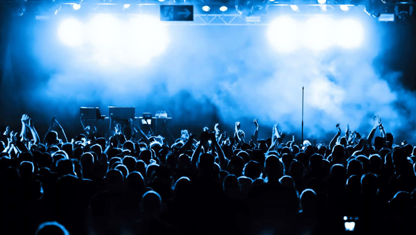 Club Party 桌布 壁紙 — 在演唱會中，剪影人群在明亮的藍色舞台燈光和煙霧下舉起雙手。