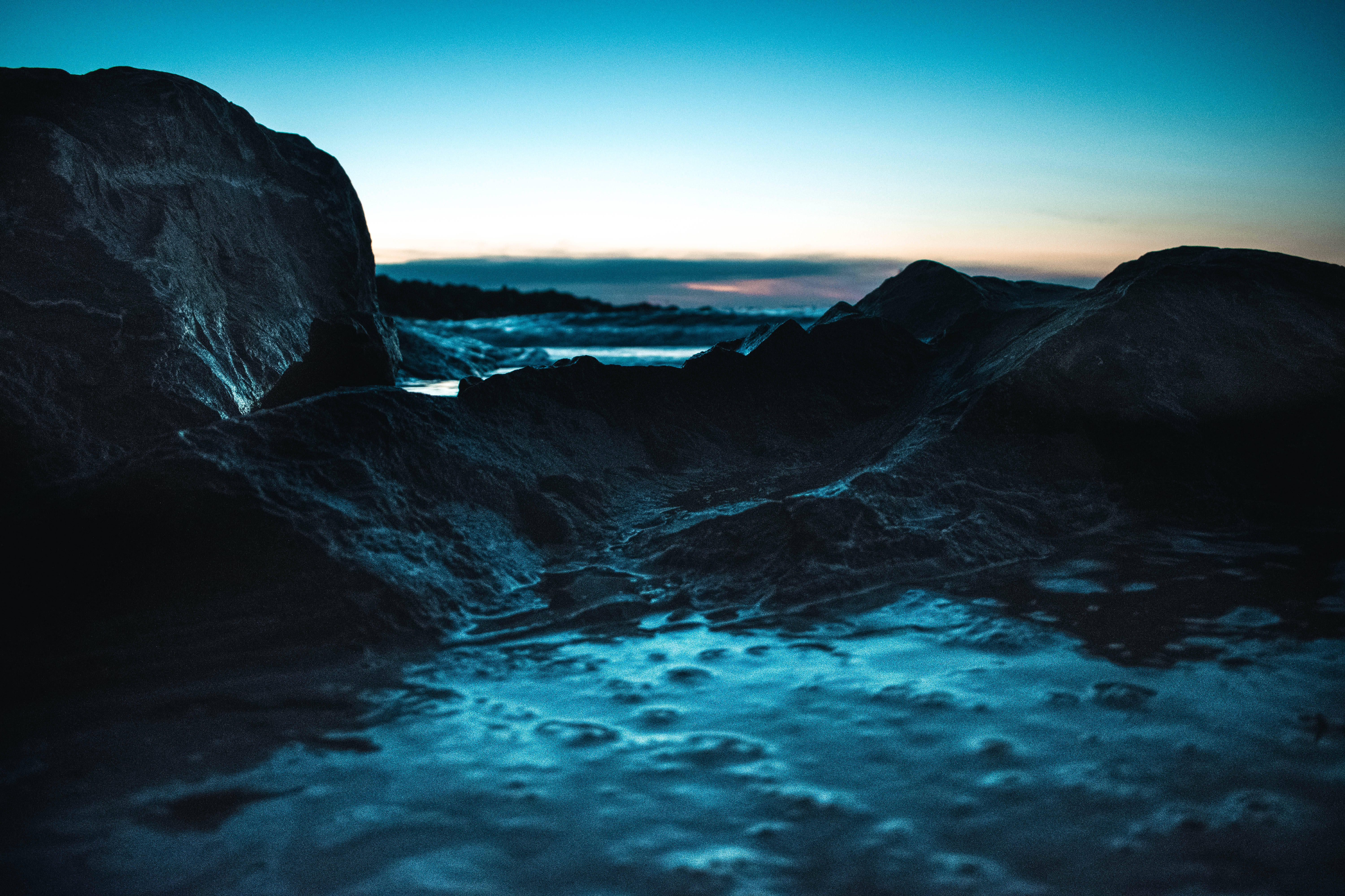 Screensavers 桌布 壁紙 — 在漸層藍天下，一個寧靜的黃昏海灘場景，有深色岩石和泡沫波浪。