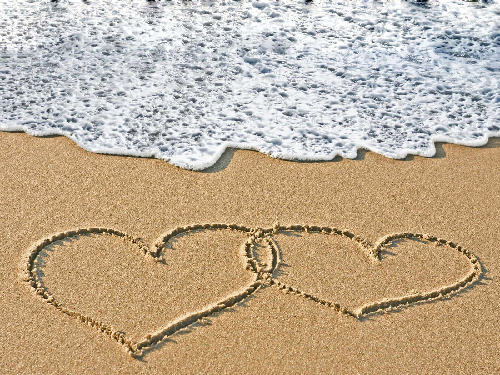 Beach Love 桌布 壁紙 — 在濕沙上畫出兩個交織的心形，溫柔的海浪緩緩湧入。