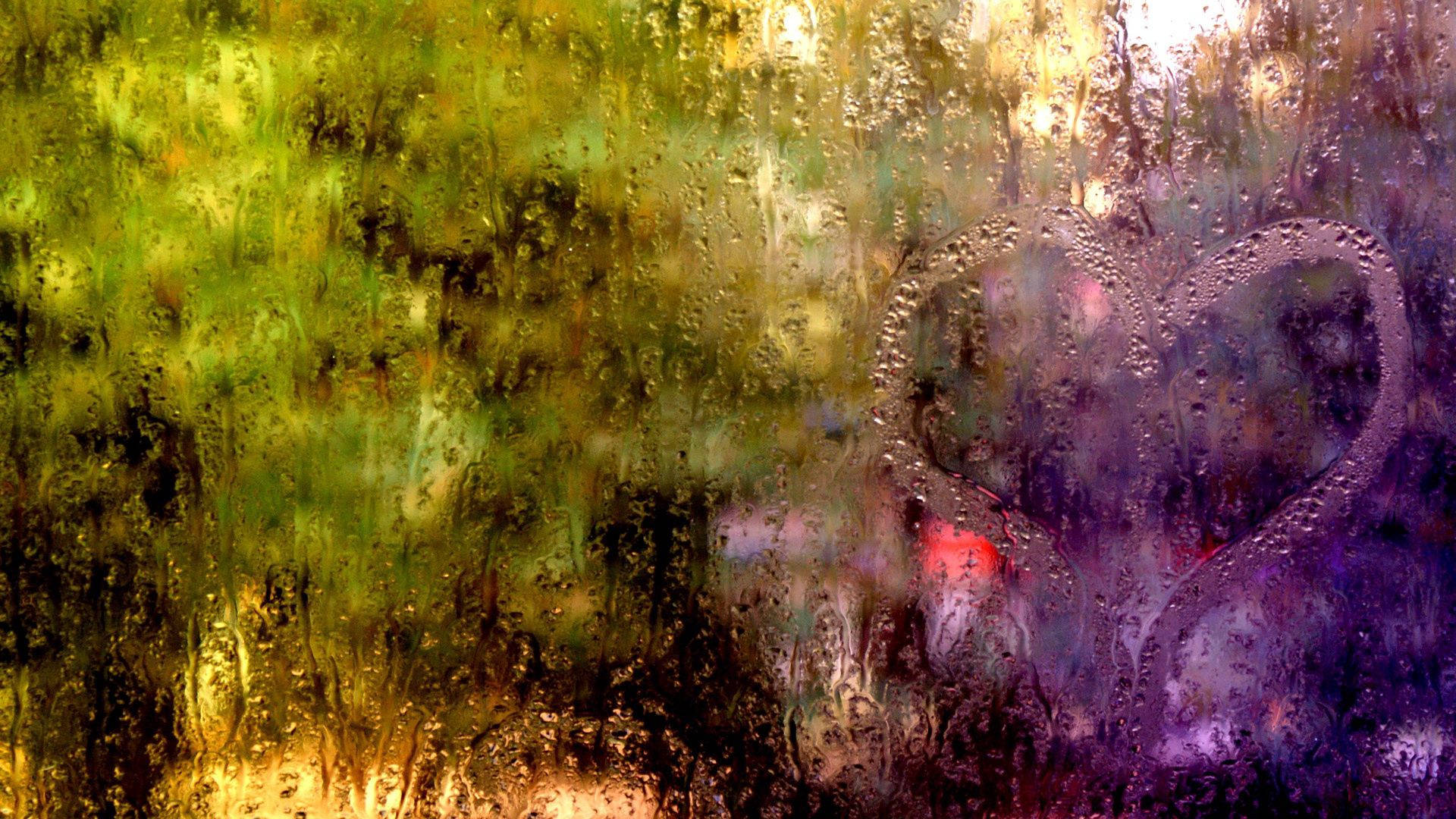 下雨 桌布 壁紙 — 在濺滿雨水的窗戶上畫的心形，外面有模糊的綠色和紫色樹葉。