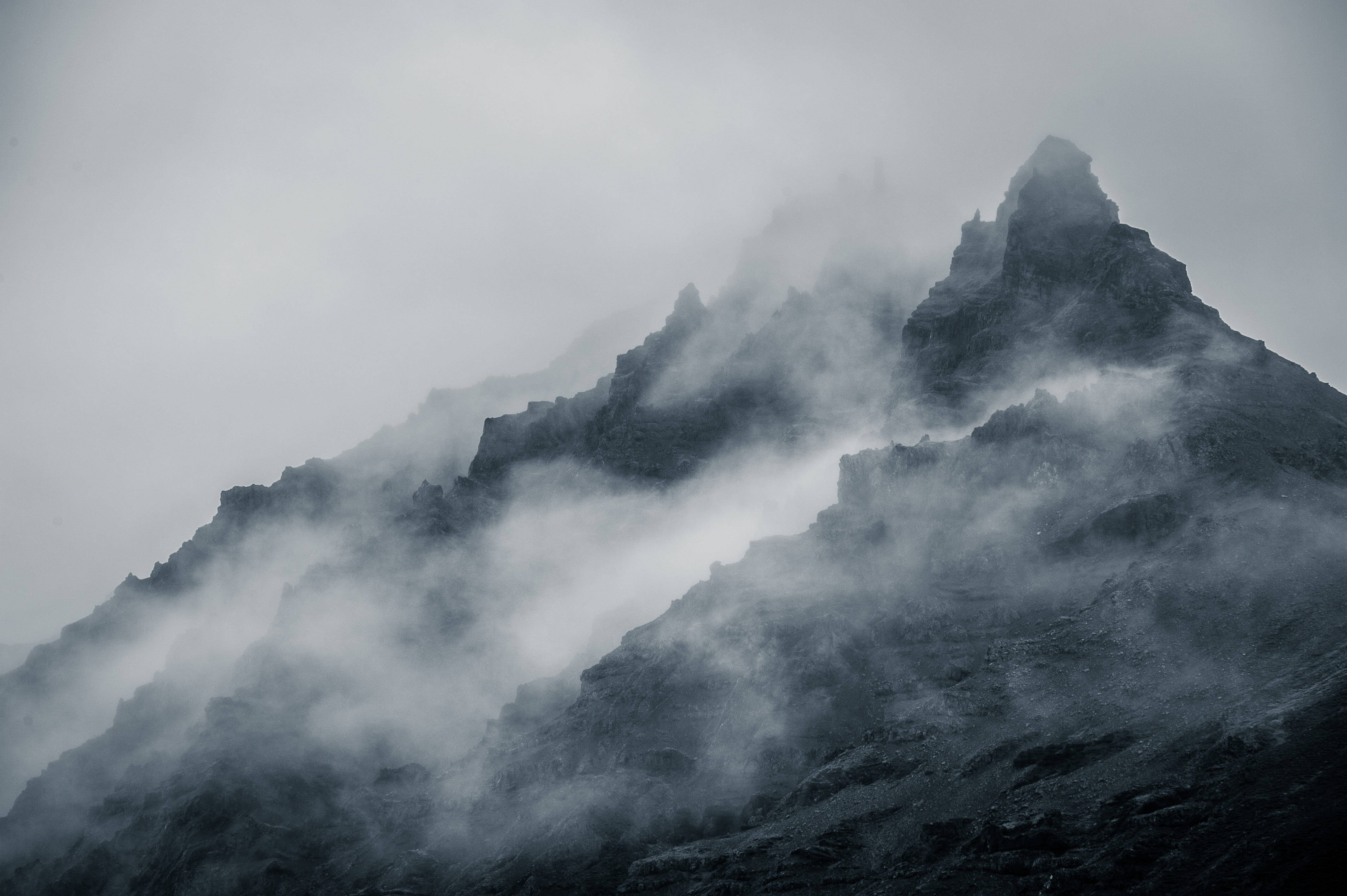 山景 桌布 壁紙 — 在灰色天空下，鋸齒狀的山峰穿過旋轉的迷霧，呈現出陰鬱的黑白景觀。