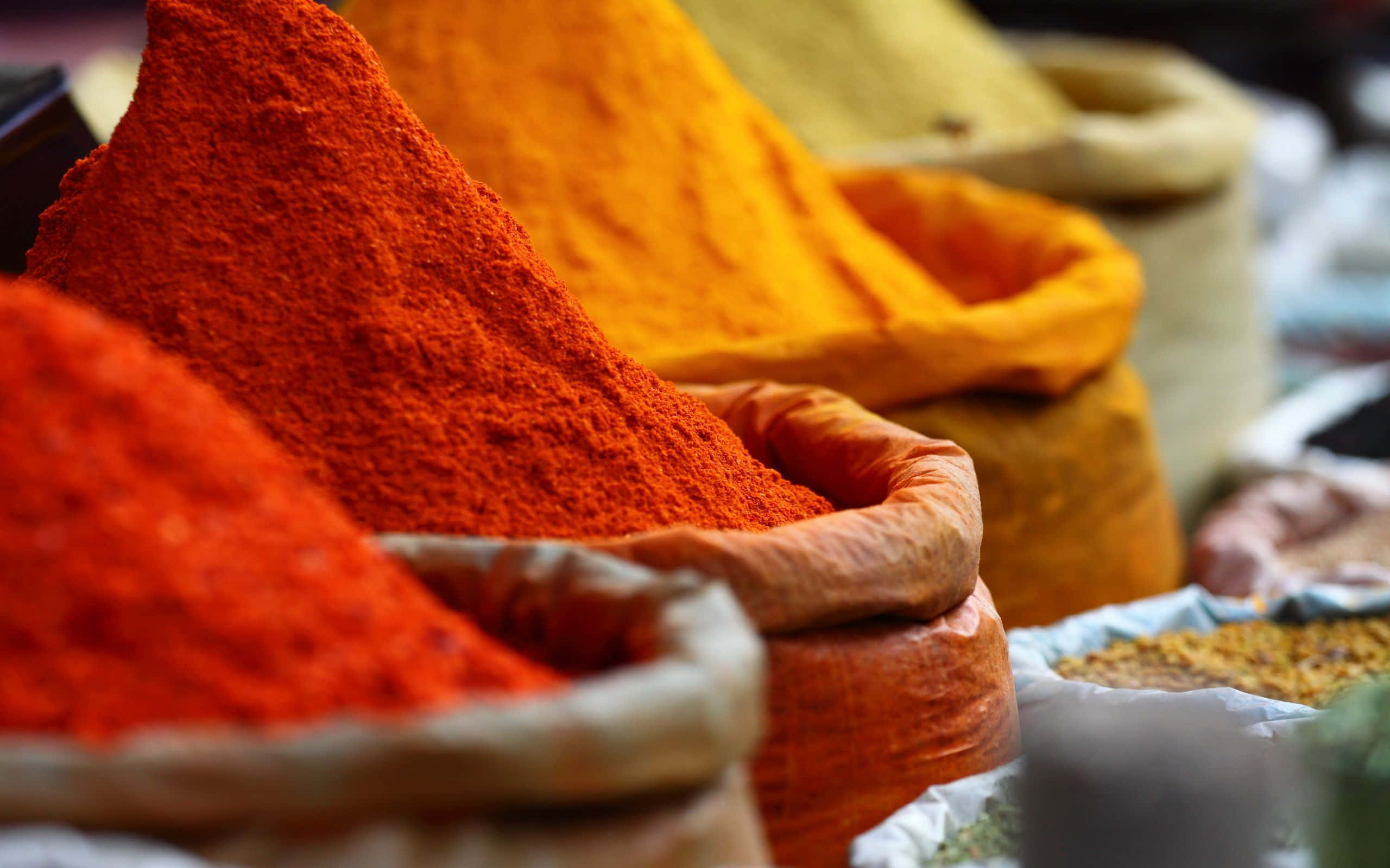 Spice 桌布 壁紙 — 在熙來攘往的市場攤位上，鮮豔的紅色、橙色和黃色香料從麻布袋中溢出。