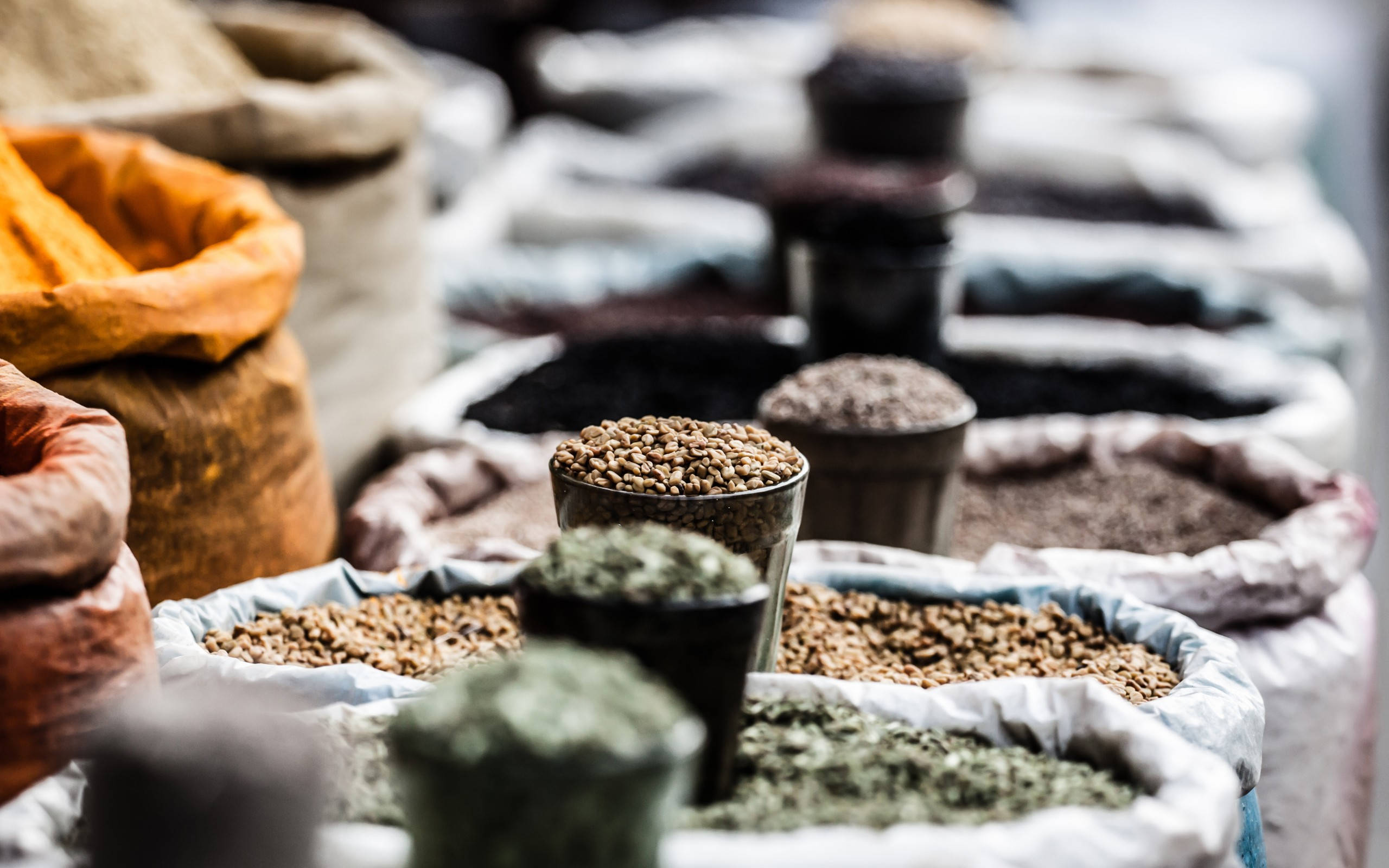 Spice 桌布 壁紙 — 在熙熙攘攘的市場攤位上，一排排色彩繽紛的香料和穀物裝在麻布袋和金屬杯中。