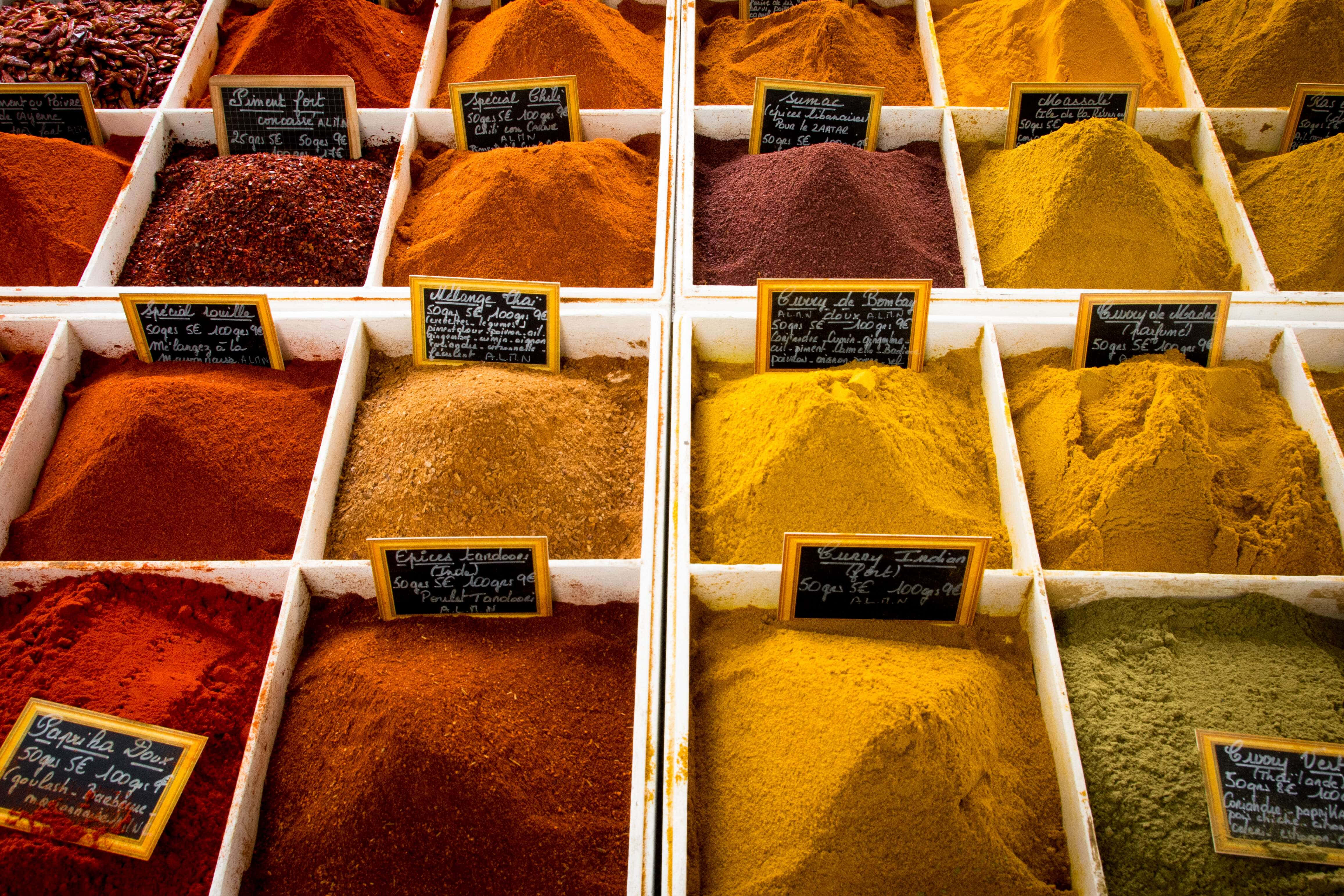 Spices 桌布 壁紙 — 在熙熙攘攘的市場攤位上，標有標籤的容器中裝滿了色彩繽紛的香料堆。