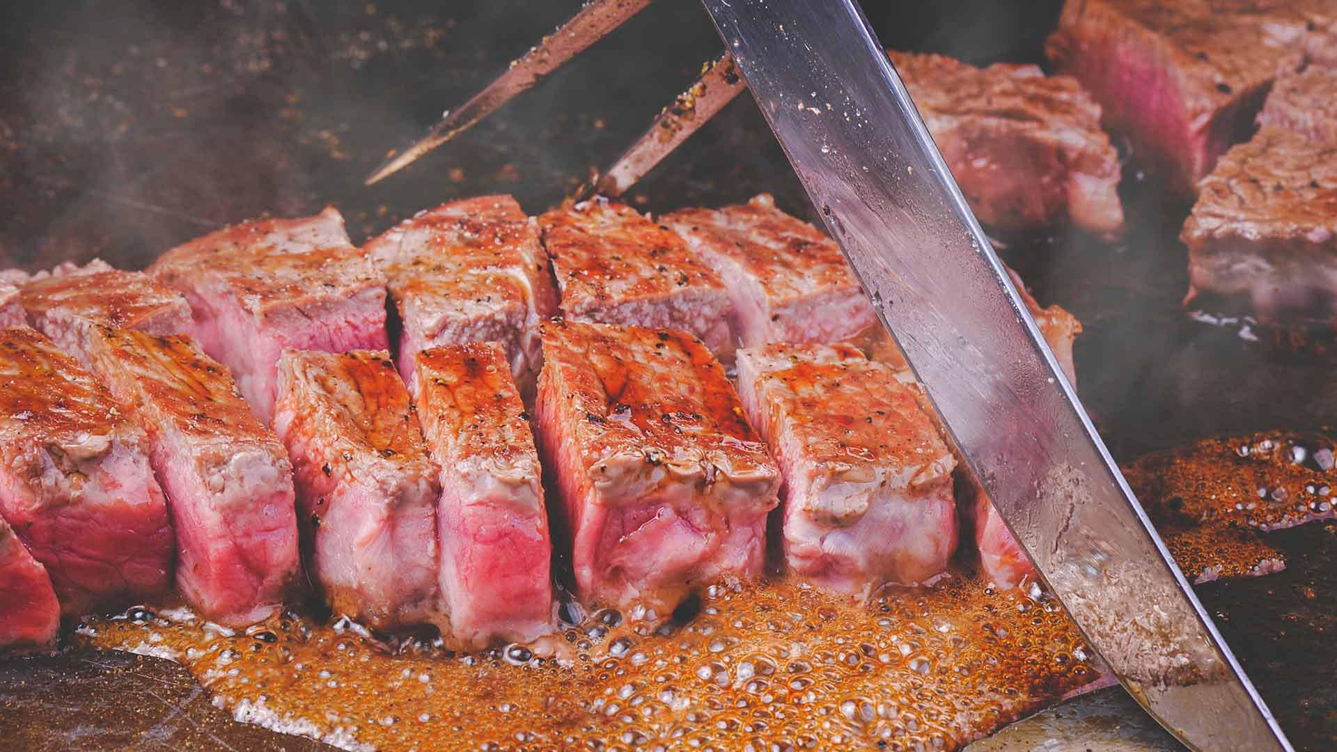 meat 桌布 壁紙 — 在熱烤架上冒著蒸氣和肉汁沸騰的同時，專業地切割著滋滋作響的三分熟牛排片。