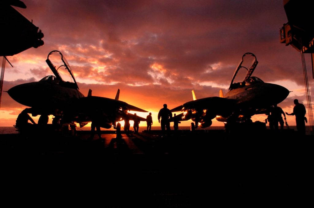 Silhouette 桌布 壁紙 — 在熾熱的日落天空背景下，航空母艦甲板上的戰鬥機和機組人員的剪影。