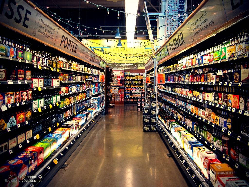 Store 桌布 壁紙 — 在燈串下，一條光線明亮的超市通道，排列著色彩繽紛的啤酒瓶和箱子。