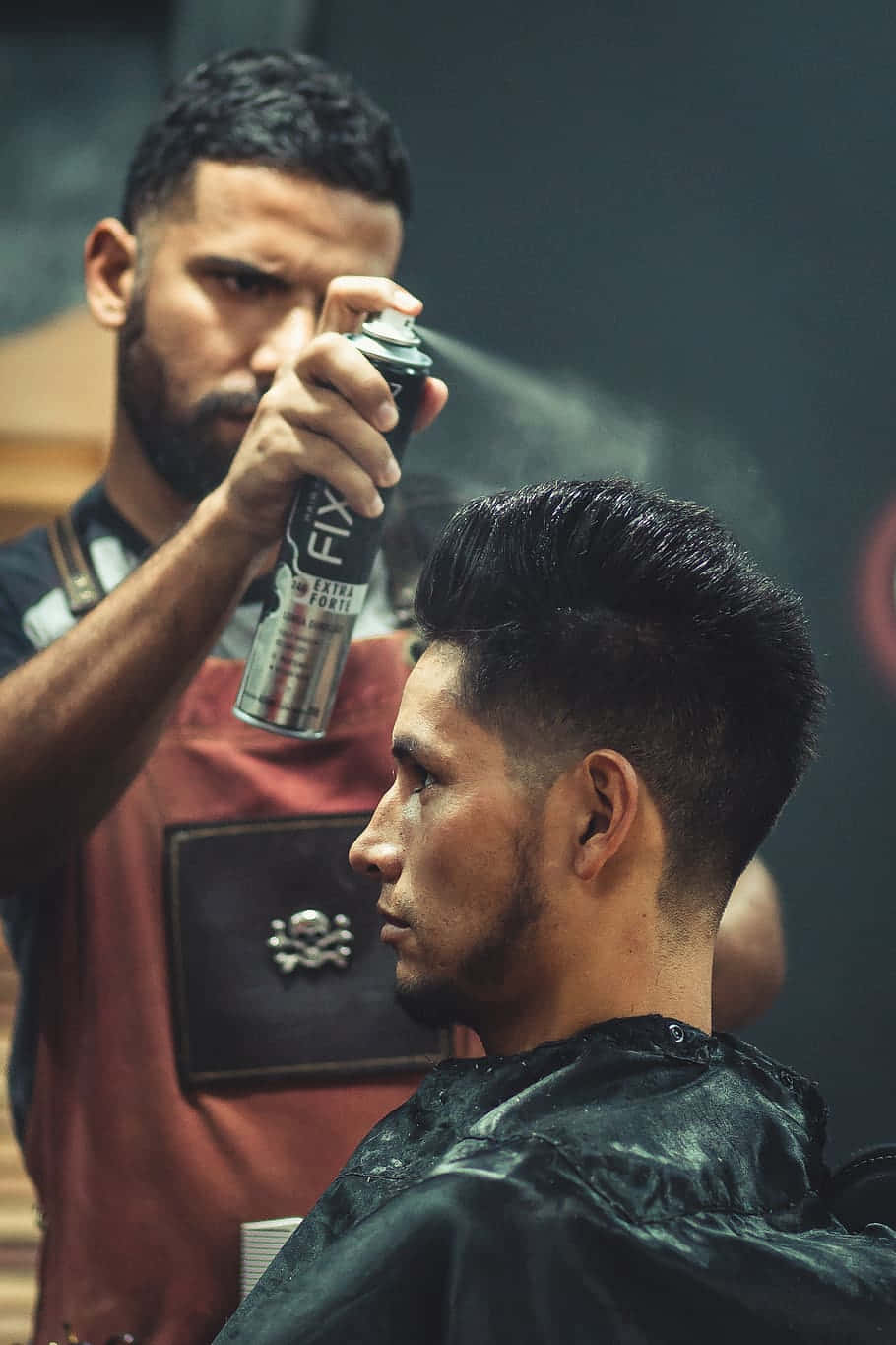Barber Shop 桌布 壁紙 — 在燈光昏暗的理髮店裡，理髮師正在為顧客剛剪好的漸層髮型噴上造型產品。