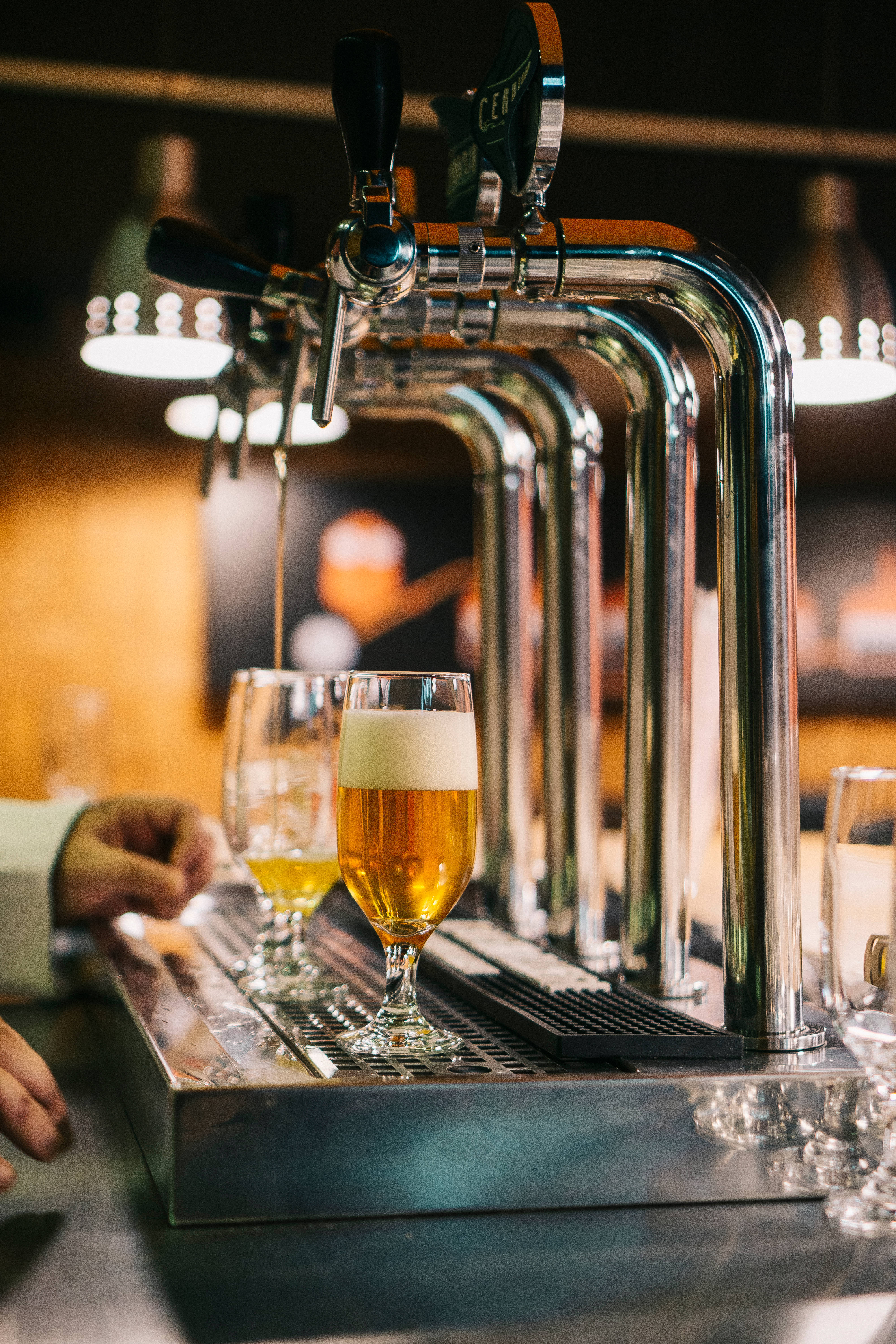 Beer 桌布 壁紙 — 在燈光昏暗的酒吧裡，一杯剛倒出的金黃色啤酒，帶有白色泡沫，放在閃閃發光的水龍頭下。