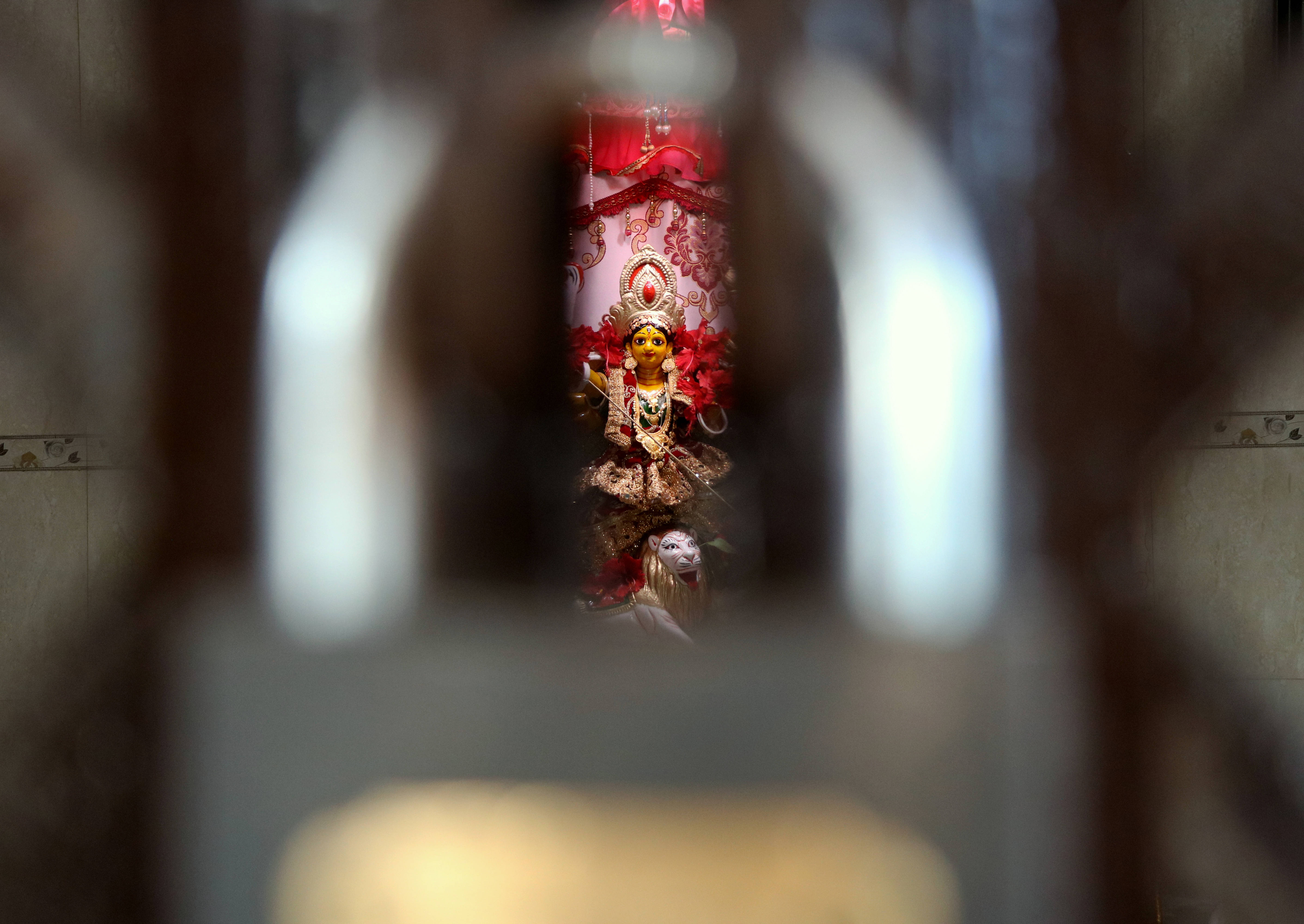 Goddess Kali 桌布 壁紙 — 在瓷磚房間中，透過模糊的裝飾金屬框架看到鮮豔的紅色和金色神像。