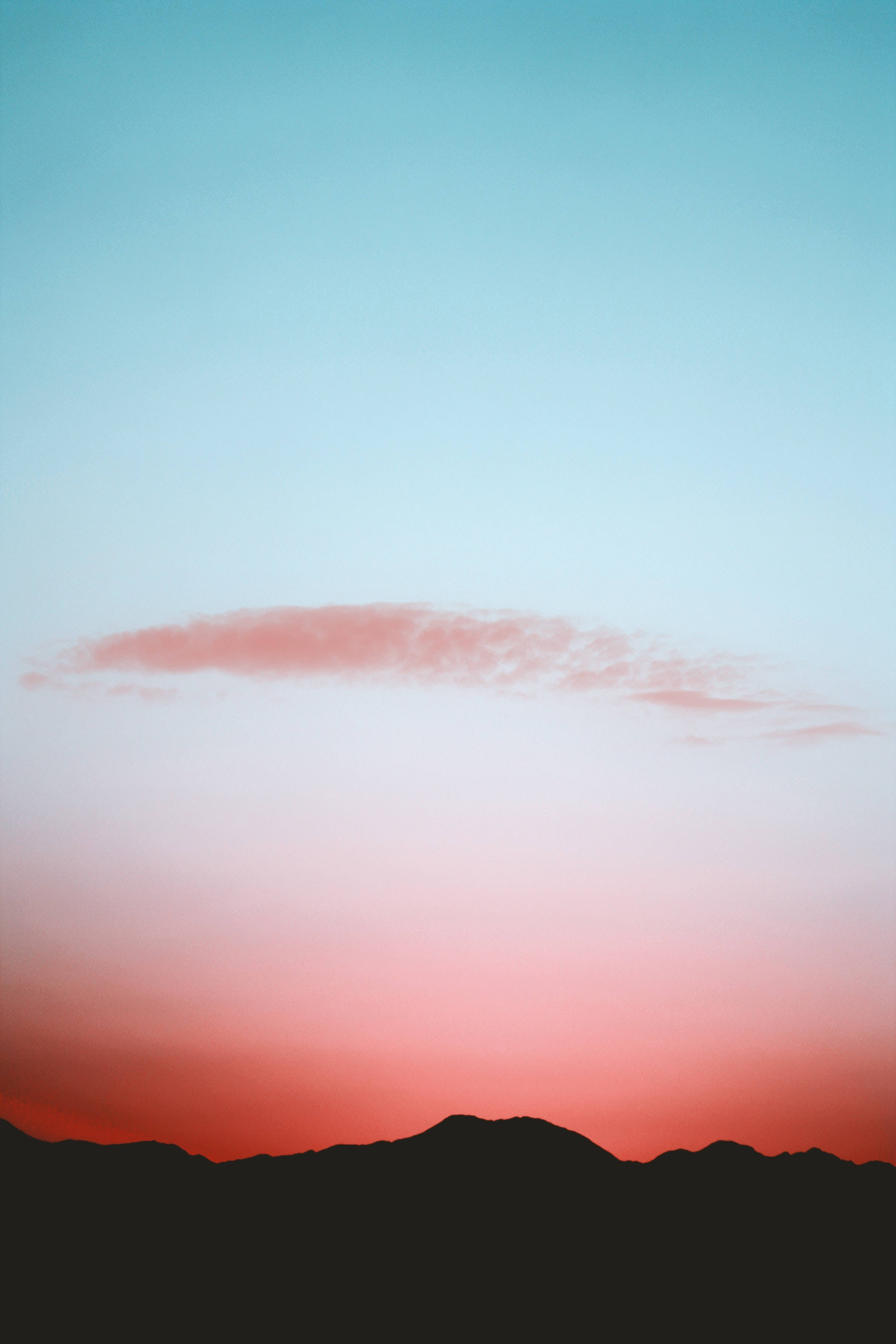 Aesthetic Sky 桌布 壁紙 — 在由珊瑚粉紅漸變至青藍色的天空下，呈現剪影的山脈，伴隨一縷薄雲。