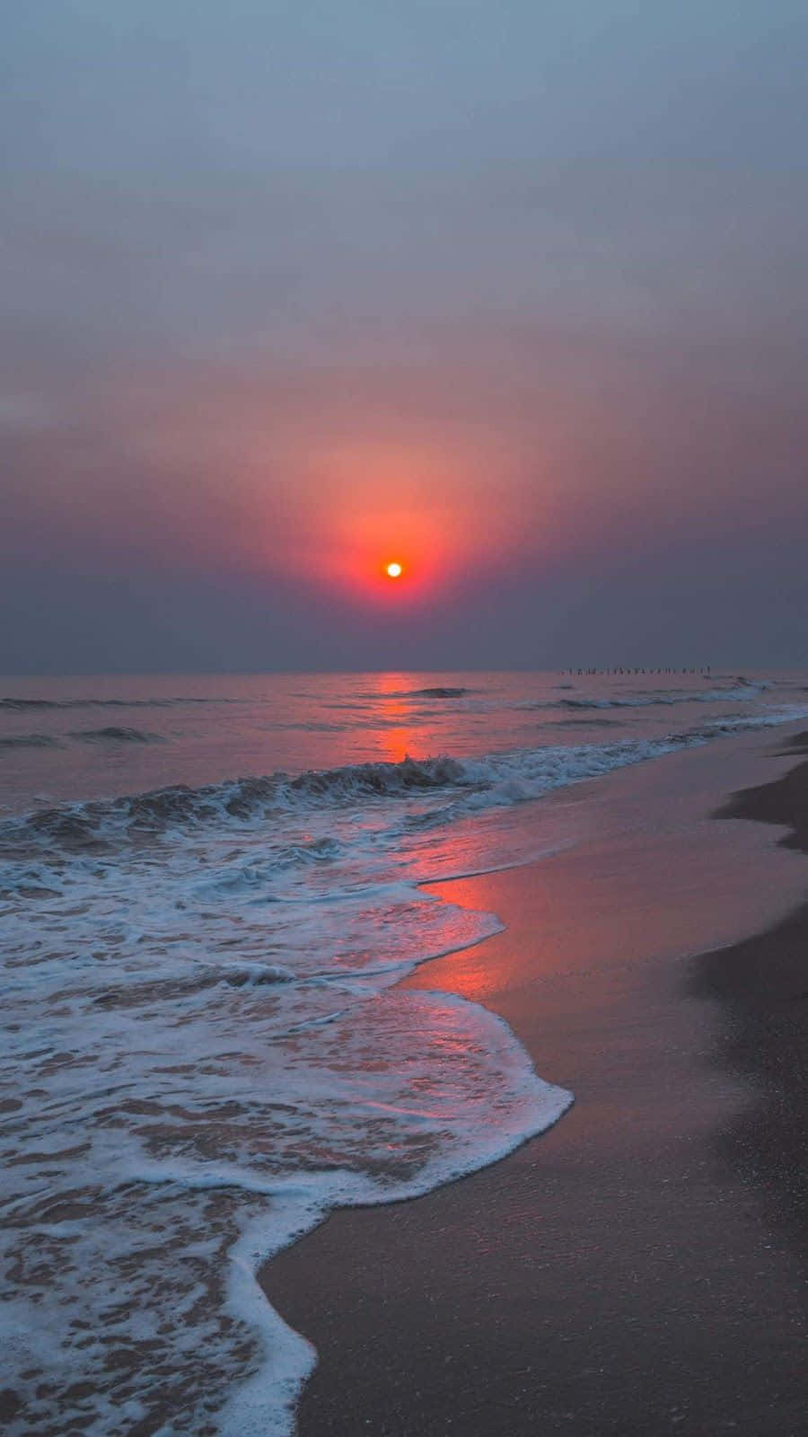 海灘日落 桌布 壁紙 — 在發光的橙色太陽下，薄霧海灘上波濤輕柔地拍打著海岸，寧靜的日落。