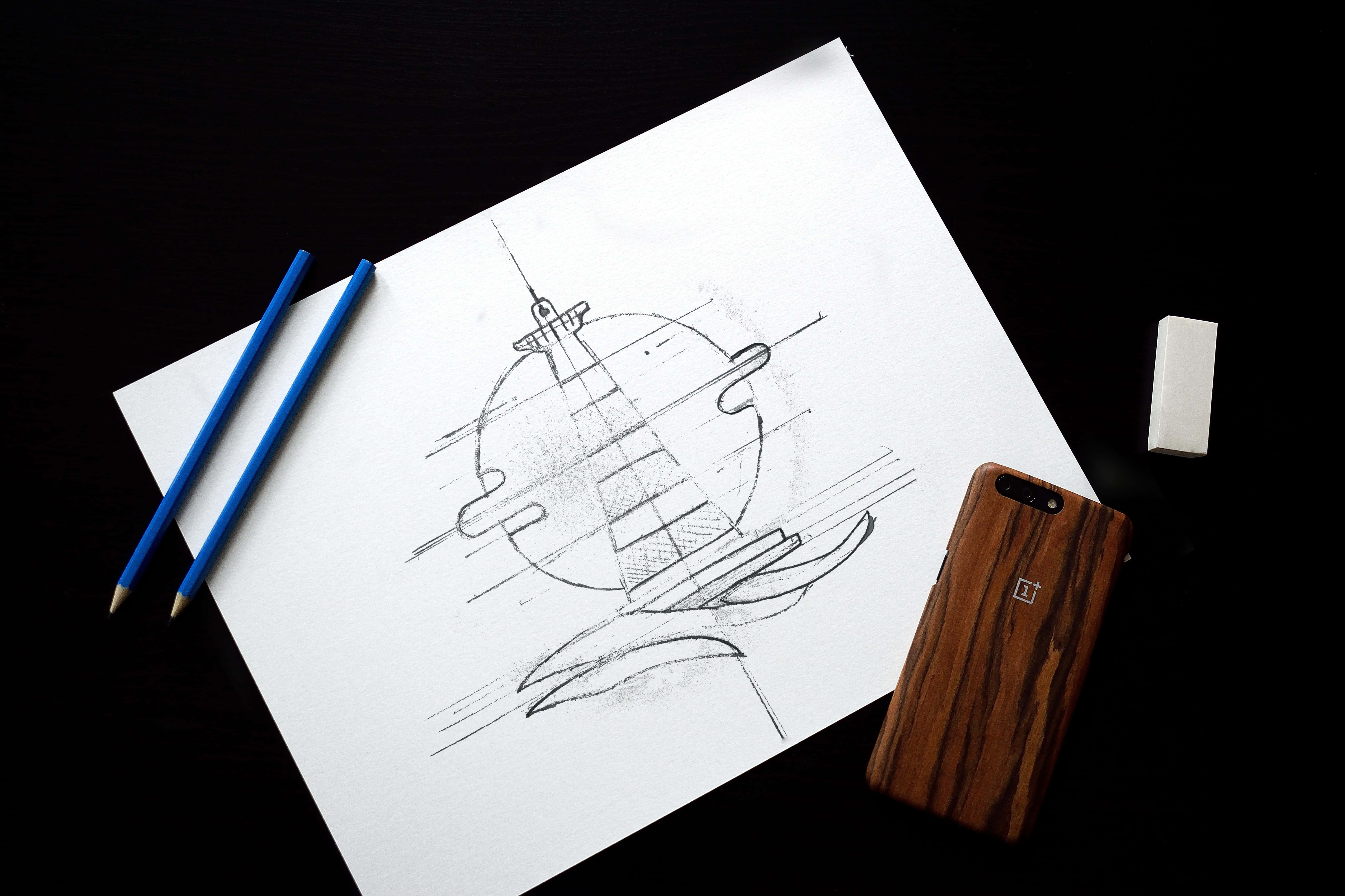 Drawing 桌布 壁紙 — 在白色紙上詳細鉛筆素描的未來太空船，旁邊有藍色鉛筆、橡皮擦和木製手機殼，置於黑色表面上。