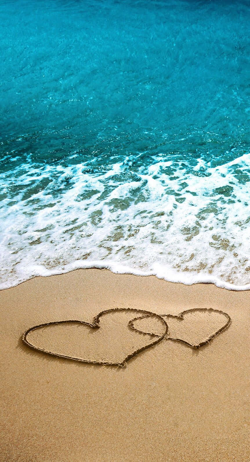 Beach Love 桌布 壁紙 — 在碧綠海洋波浪邊緣的濕沙上繪製的兩個交織心形。