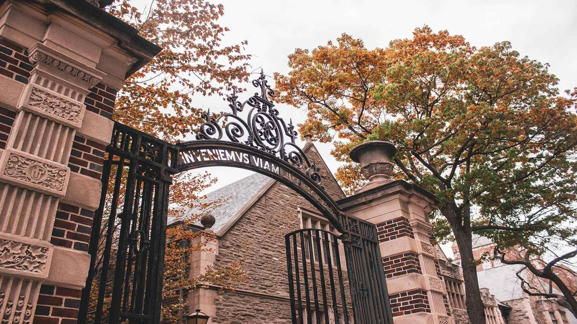 University Of Pennsylvania 桌布 壁紙 — 在秋樹下，石柱之間有一座裝飾性的黑色鐵門，帶有 'INVENIEMVS VIAM' 拱門。