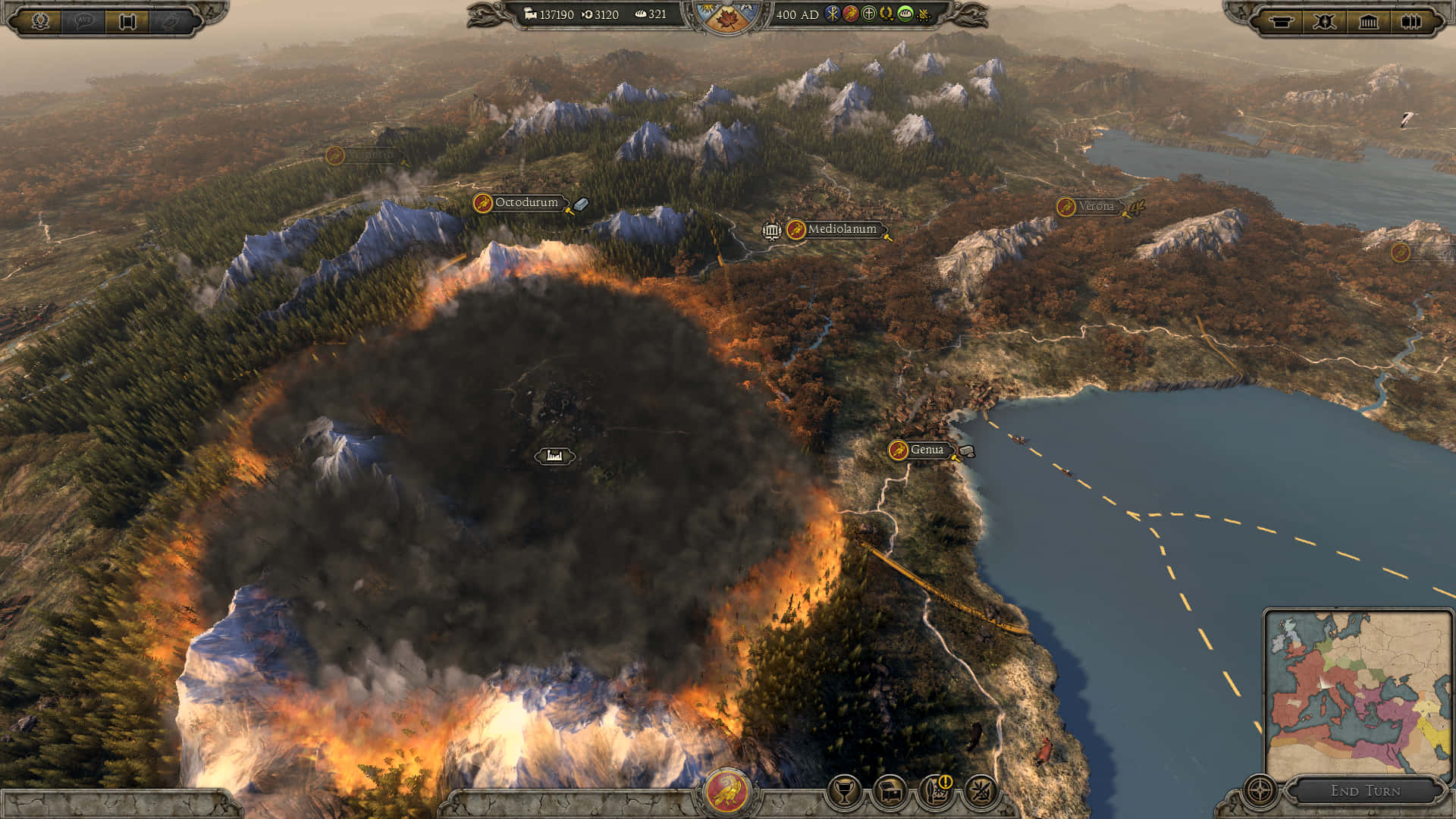 Total War Attila 桌布 壁紙 — 在策略遊戲介面中，大規模火山爆發噴出煙霧和火焰，橫跨有湖泊和定居點的山區景觀。
