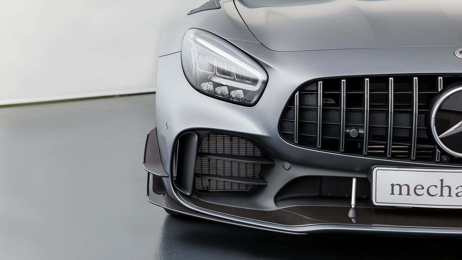 汽車 桌布 壁紙 — 在簡約工作室環境中，時尚銀色 Mercedes-AMG 跑車的前格柵和頭燈特寫。