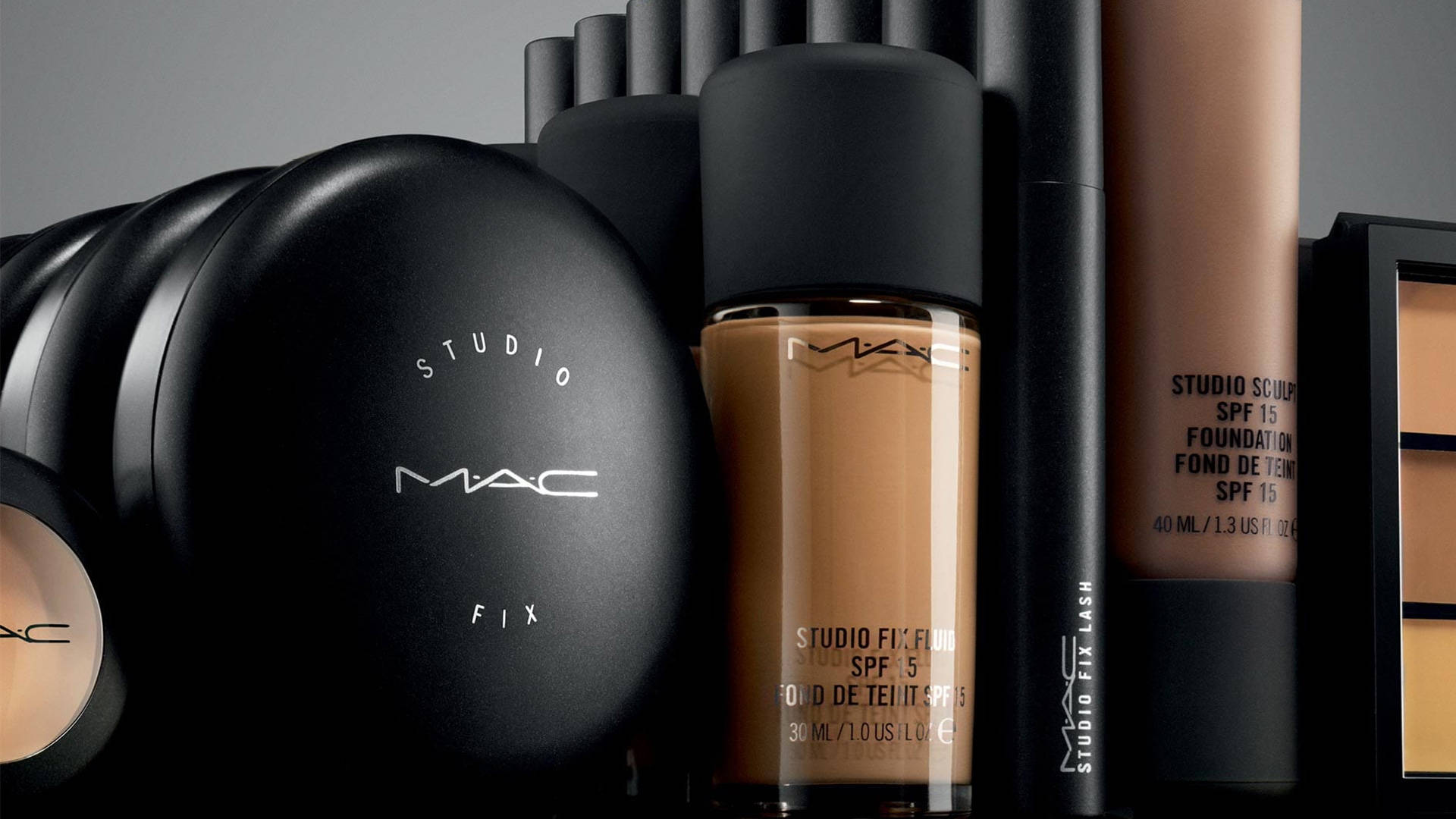 Cosmetics 桌布 壁紙 — 在簡約灰色背景上，黑色和米色調的MAC Studio Fix化妝產品的時尚排列。