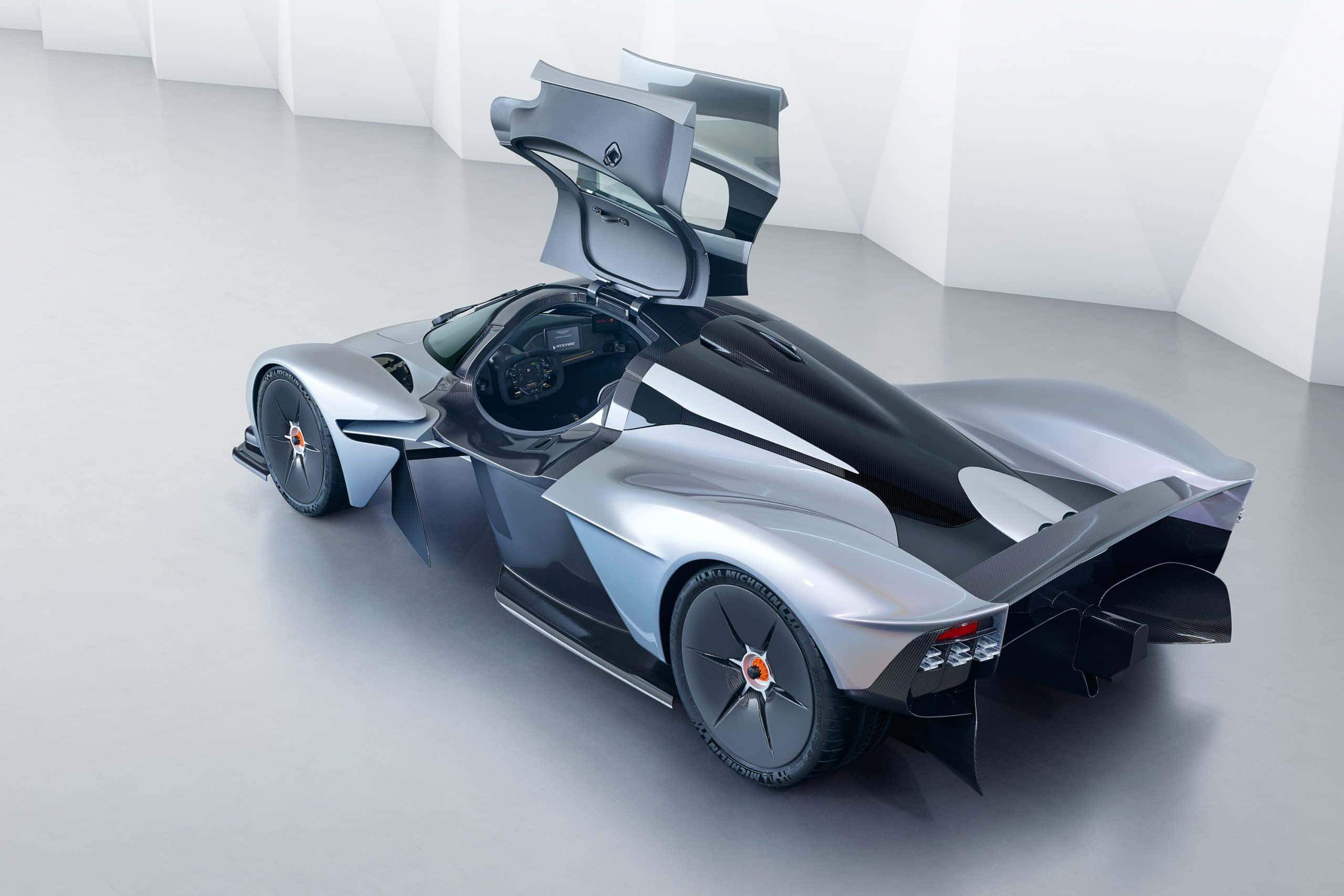 Aston Martin Valkyrie 桌布 壁紙 — 在簡約白色工作室中，一輛時尚的銀黑未來主義跑車，鷗翼門打開。